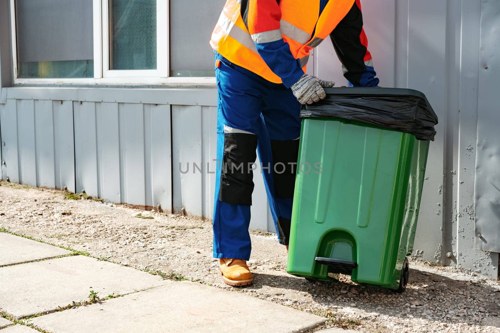 Male janitor in uniform cleans a trash can in the street close up