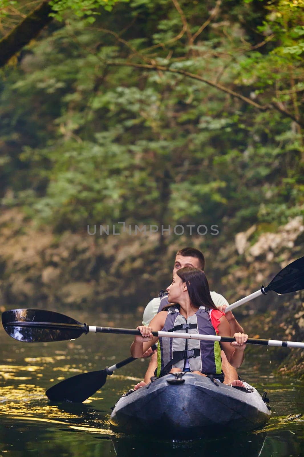 A young couple enjoying an idyllic kayak ride in the middle of a beautiful river surrounded by forest greenery.