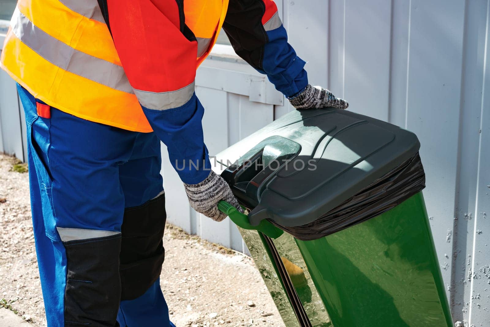 Male janitor in uniform cleans a trash can in the street close up