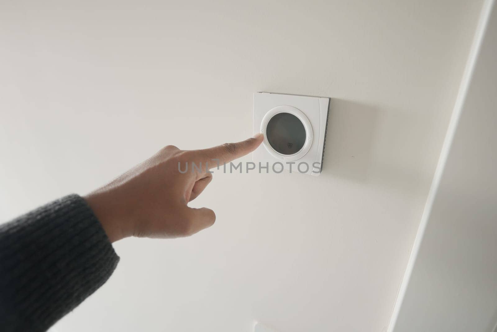 Hand adjusting smart home thermostat on white wall, displaying modern technology and interior system