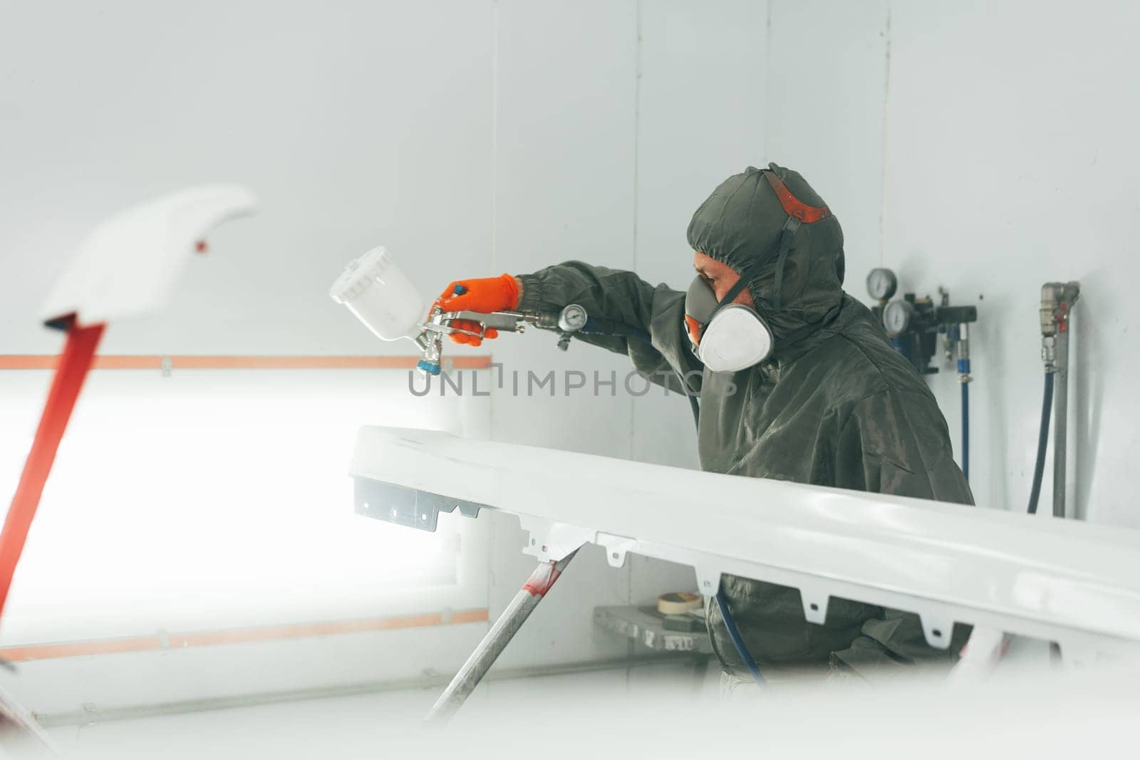 Auto mechanic worker wearing protective workwear spraying white paint on car part at workshop close up