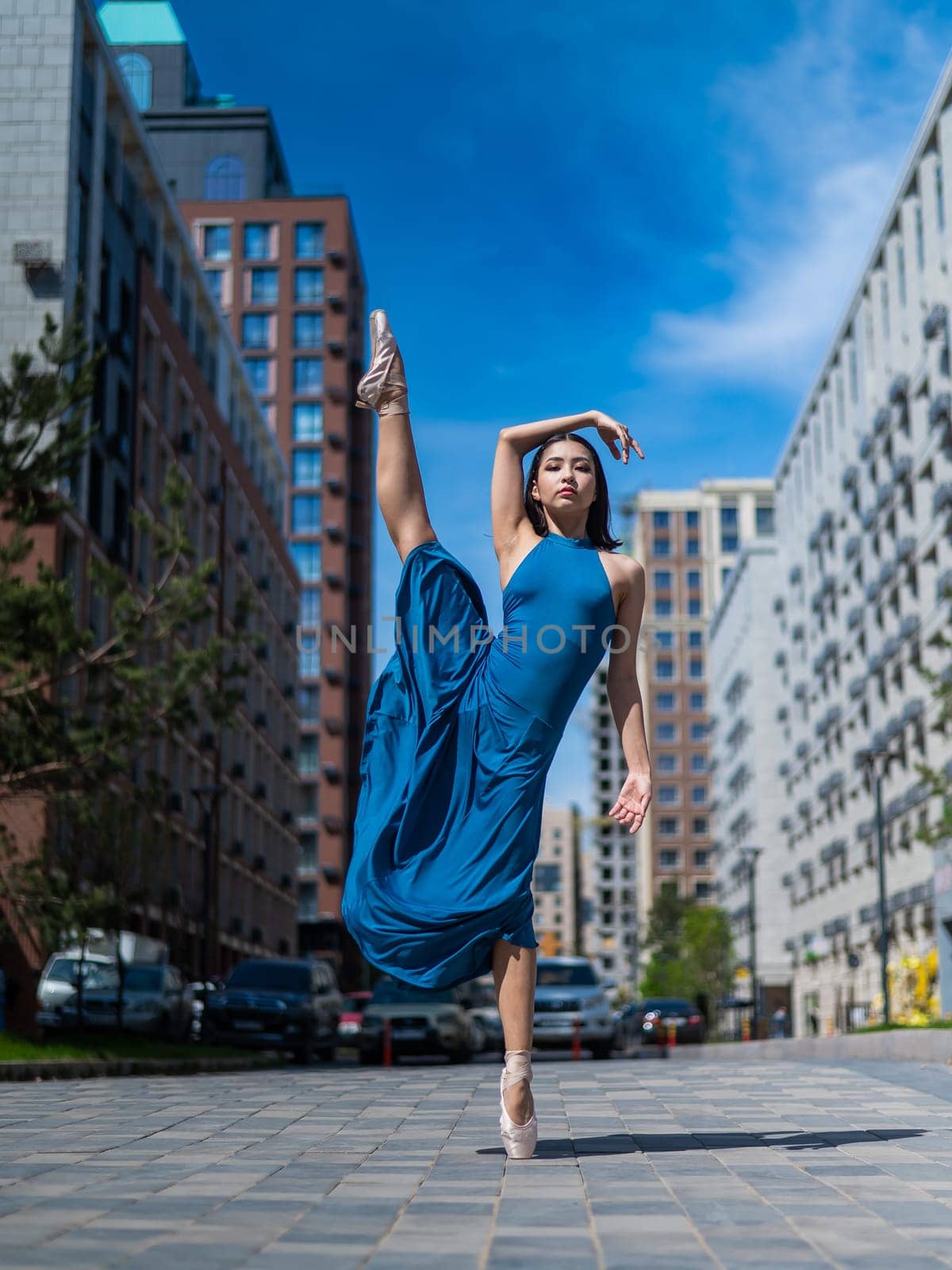 Beautiful Asian ballerina in blue dress posing in splits outdoors. Urban landscape. Vertical photo. by mrwed54