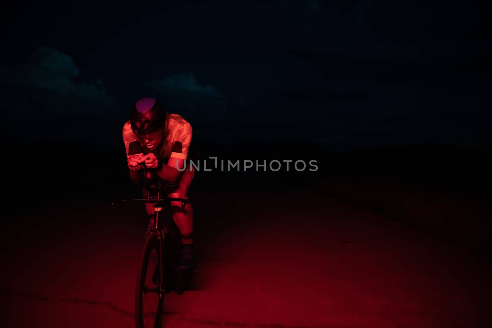 A triathlete rides his bike in the darkness of night, pushing himself to prepare for a marathon. The contrast between the darkness and the light of his bike creates a sense of drama and highlights the athlete's determination and perseverance