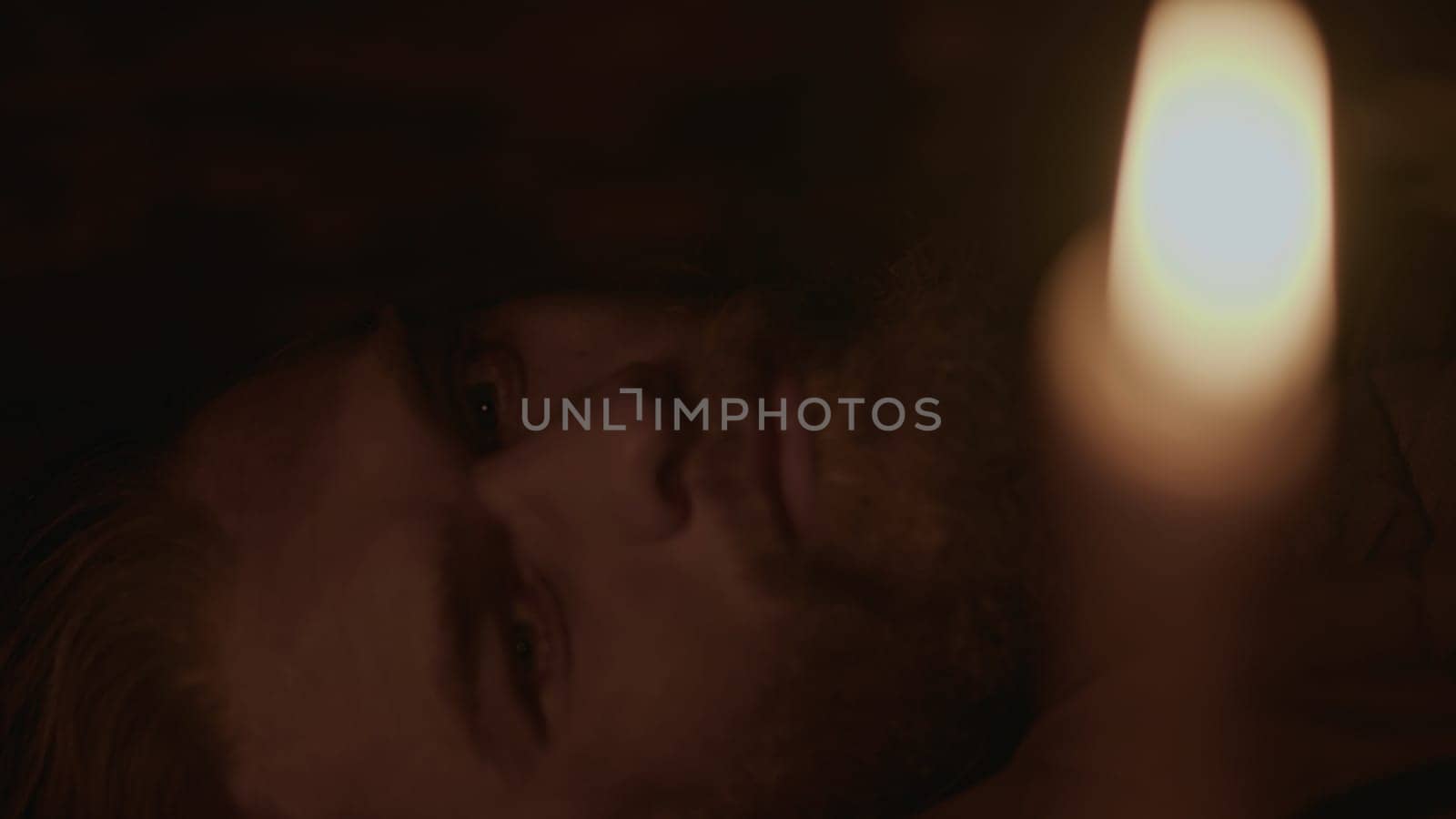 Close up of young bearded man closing eyes and falling asleep in a dark room with candlelight. Media. Pensive man lying and sleeping at night indoors