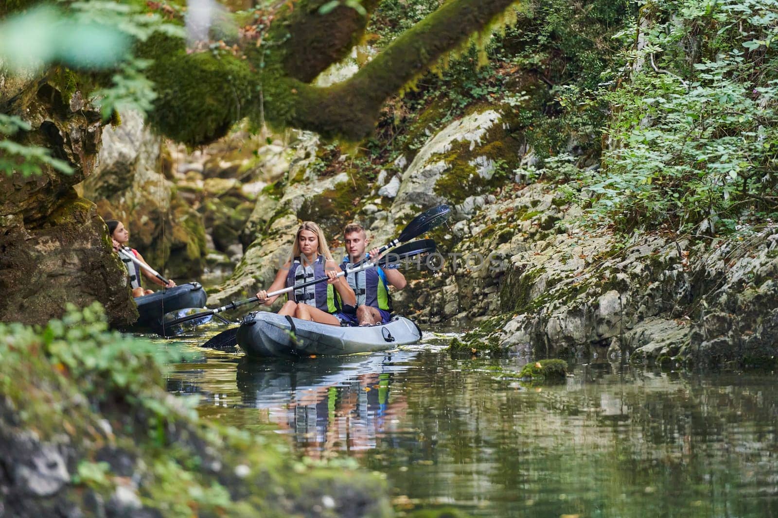 A young couple enjoying an idyllic kayak ride in the middle of a beautiful river surrounded by forest greenery.