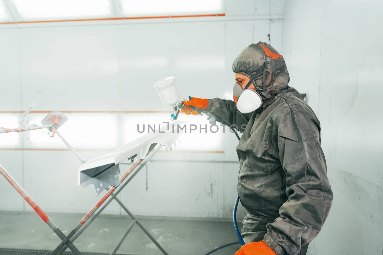 Auto painter painting a car with vaporizer gun inside a paint booth close up