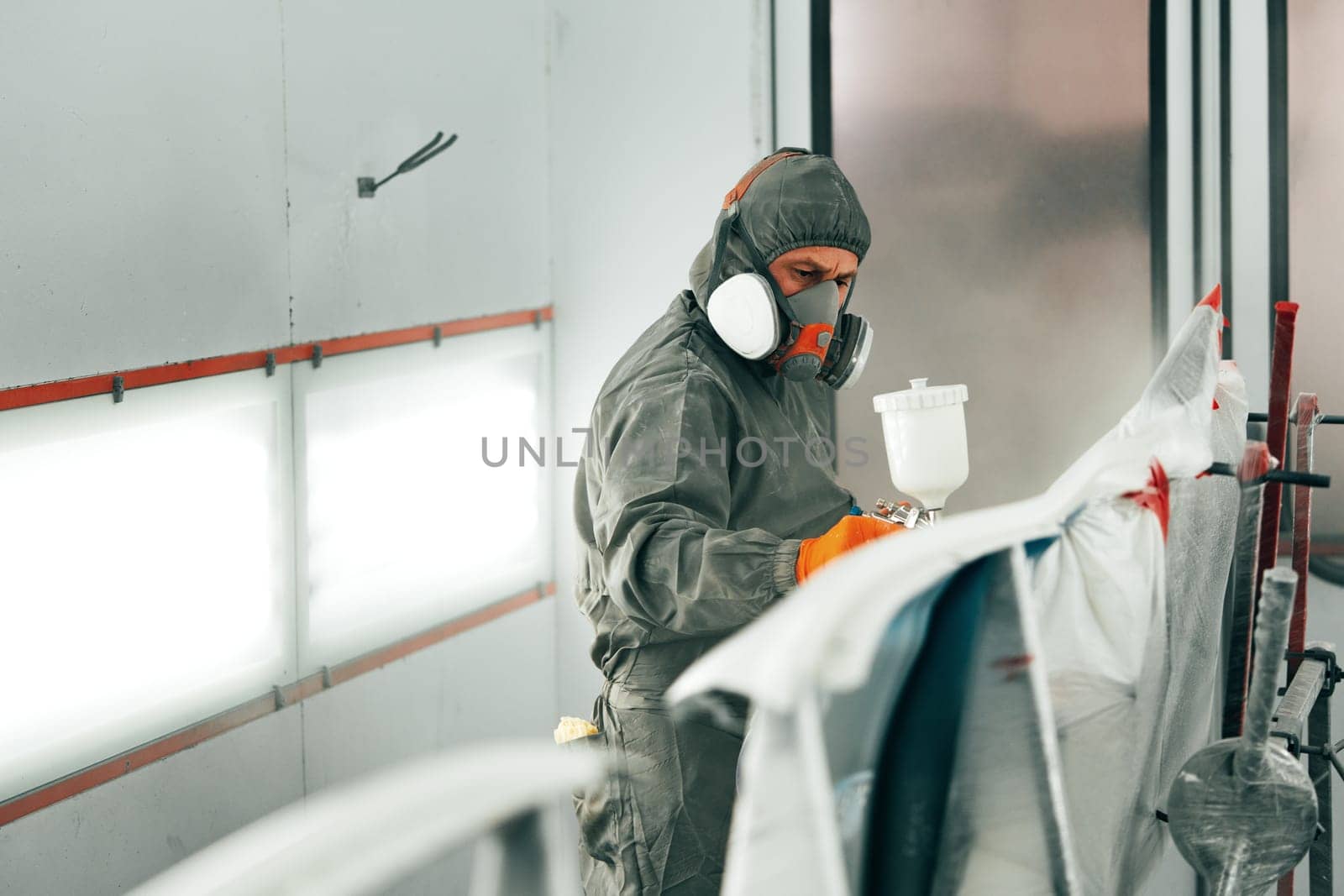 Auto painter painting a car with vaporizer gun inside a paint booth close up