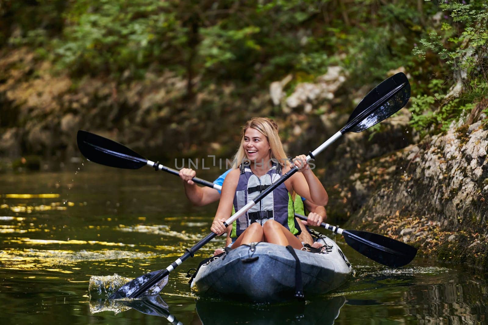 A young couple enjoying an idyllic kayak ride in the middle of a beautiful river surrounded by forest greenery by dotshock