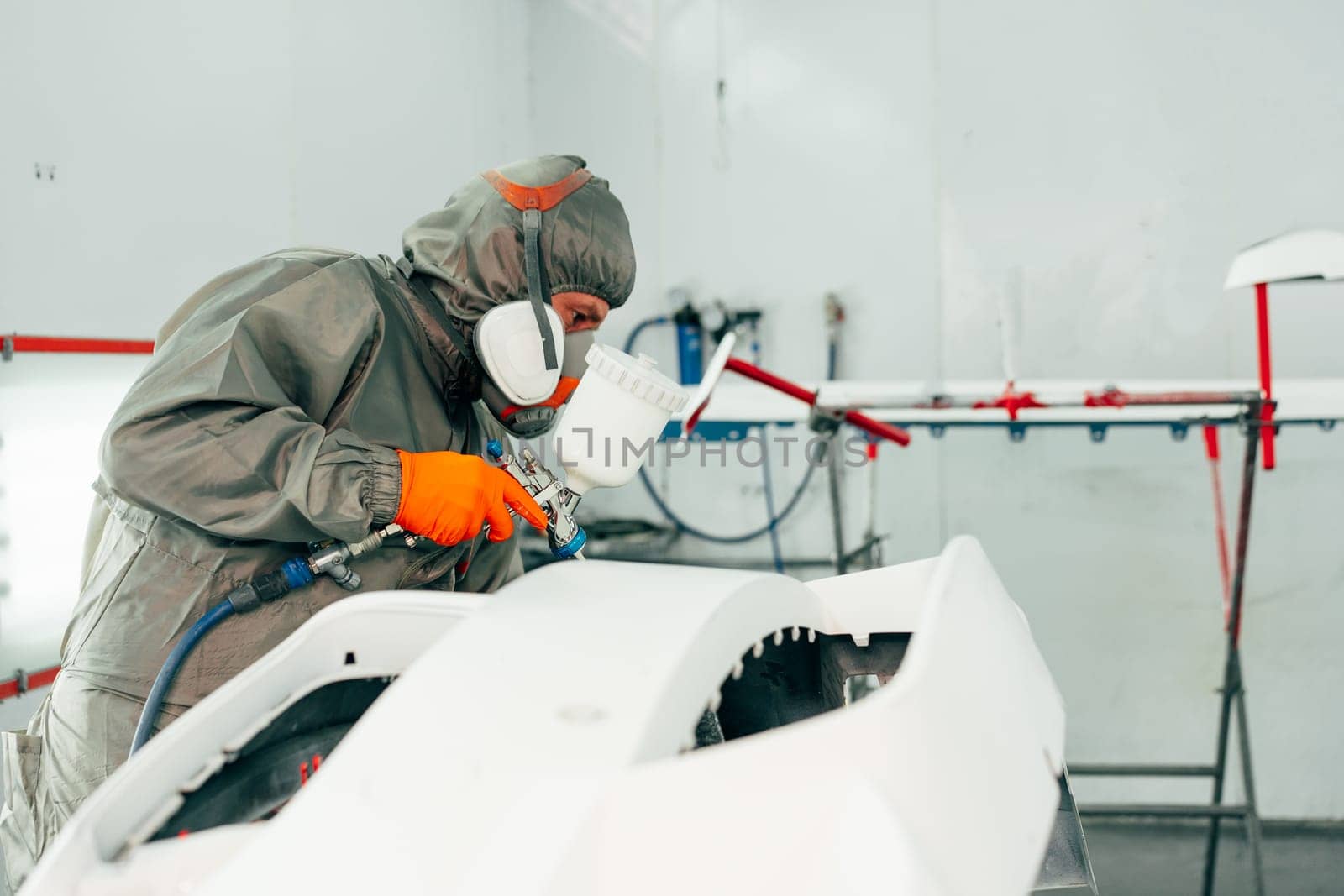 Auto mechanic worker wearing protective workwear spraying white paint on car part at workshop close up