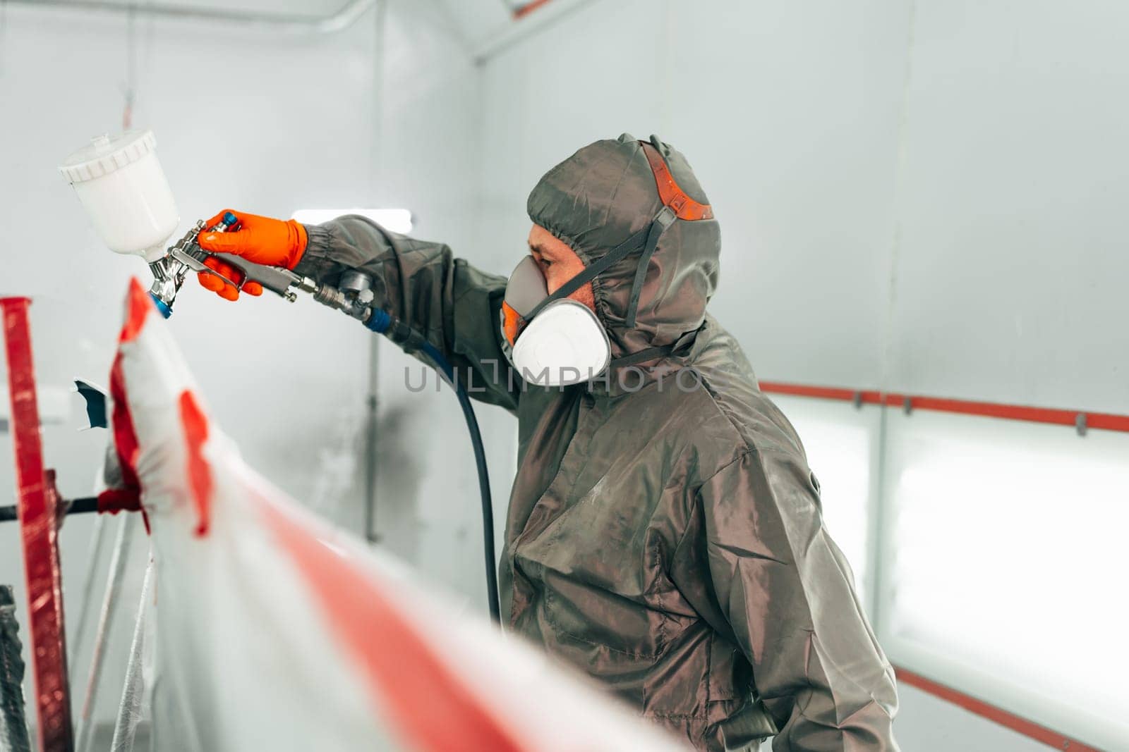 Auto mechanic worker wearing protective workwear spraying white paint on car part at workshop close up