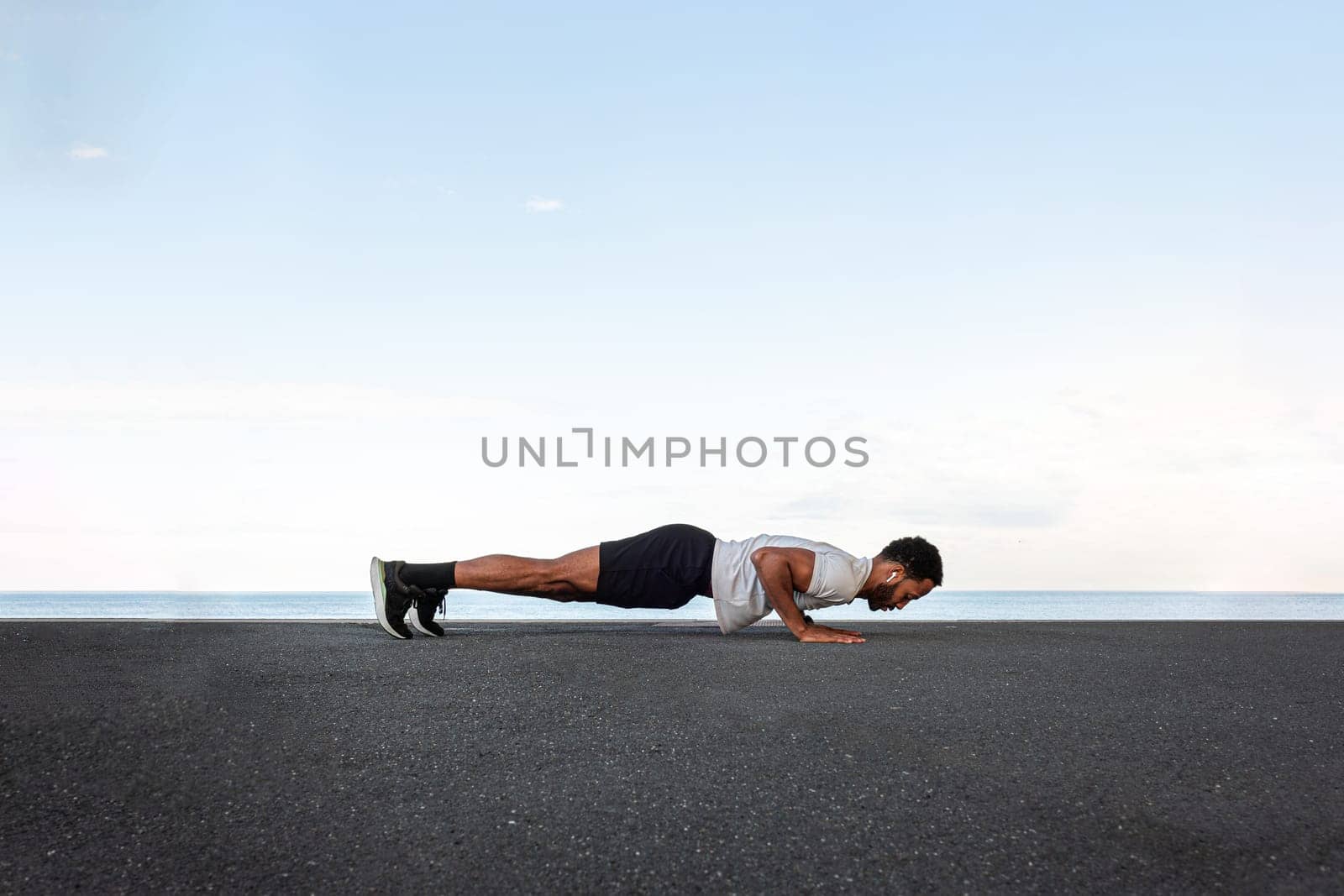 Side view of young African American male wearing sportswear doing push ups outdoors. Copy space. Active and healthy lifestyle concept.