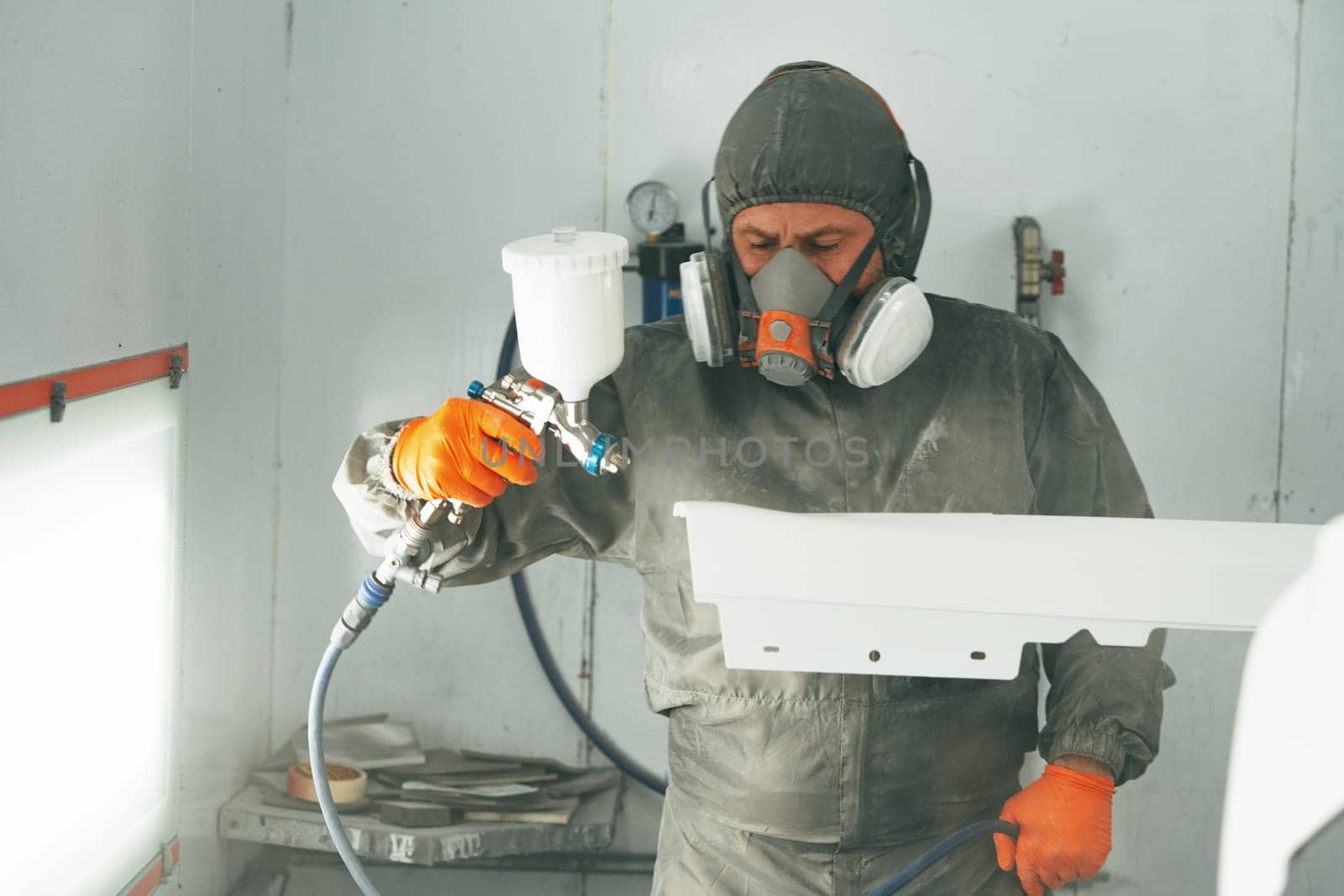 Auto painter painting a car with vaporizer gun inside a paint booth close up