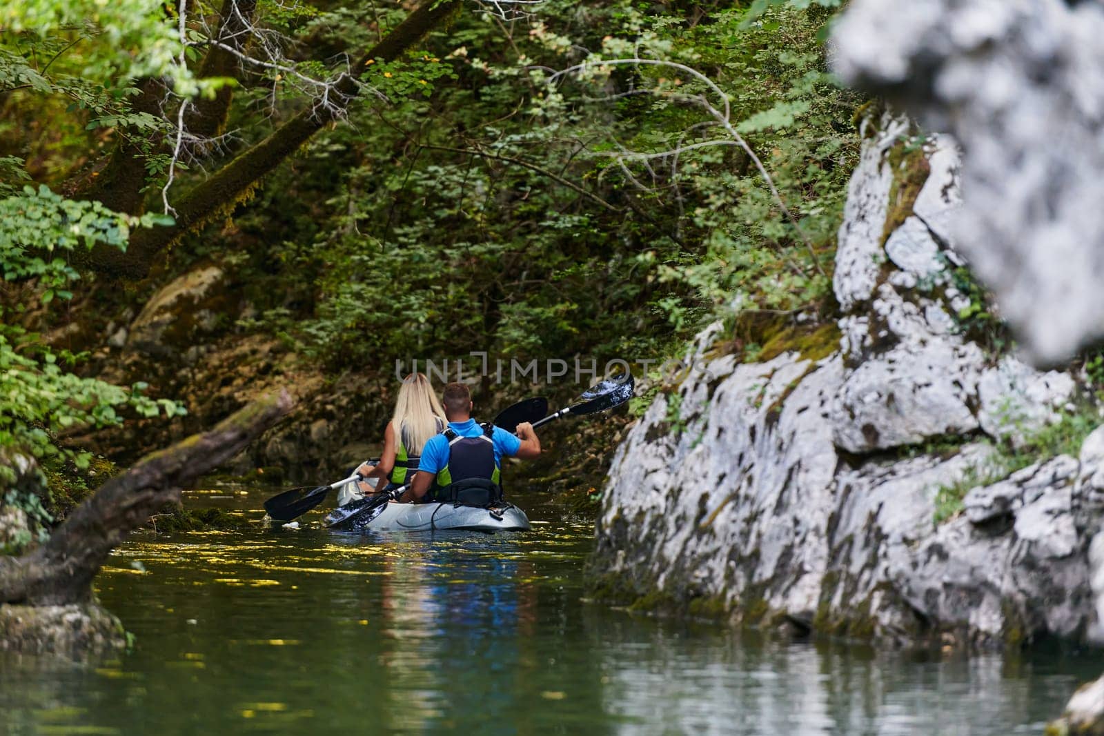 A young couple enjoying an idyllic kayak ride in the middle of a beautiful river surrounded by forest greenery by dotshock