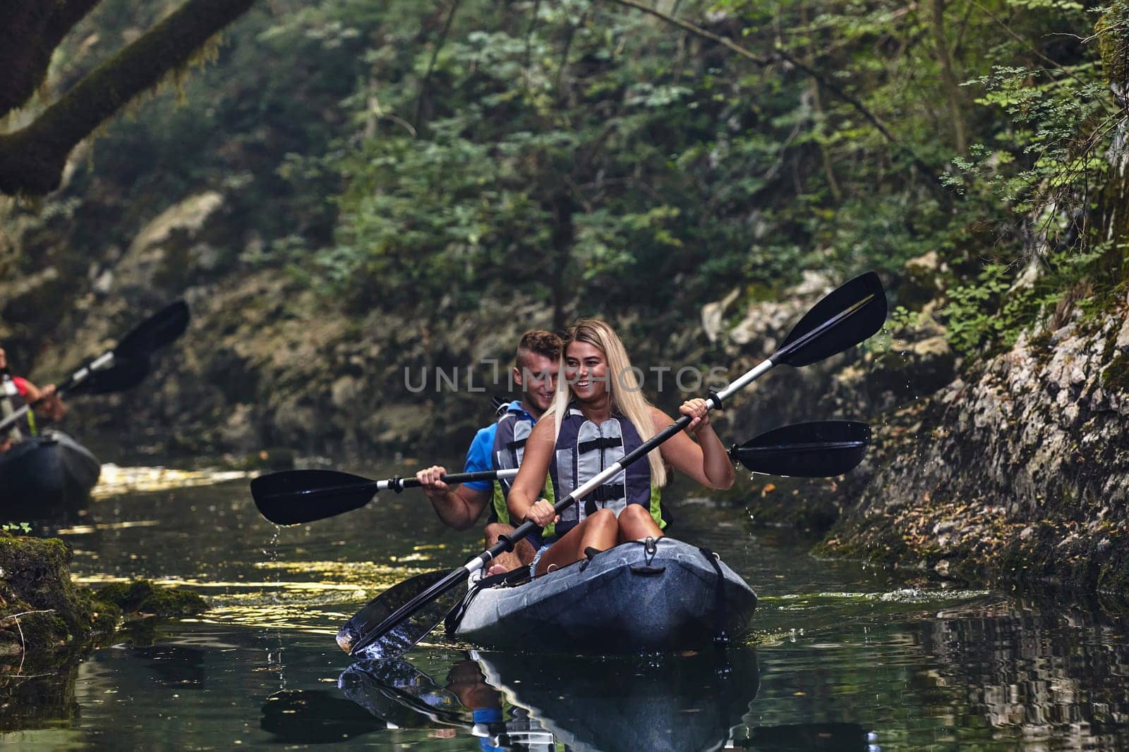 A group of friends enjoying having fun and kayaking while exploring the calm river, surrounding forest and large natural river canyons by dotshock