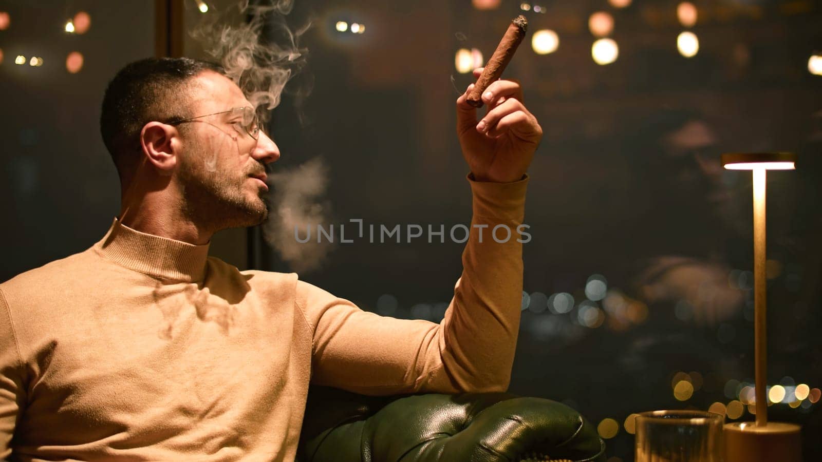 Businessman smokes cigar in restaurant. Media. Man smokes cigar in luxury restaurant at night. Elegant man smokes cigar in evening restaurant.