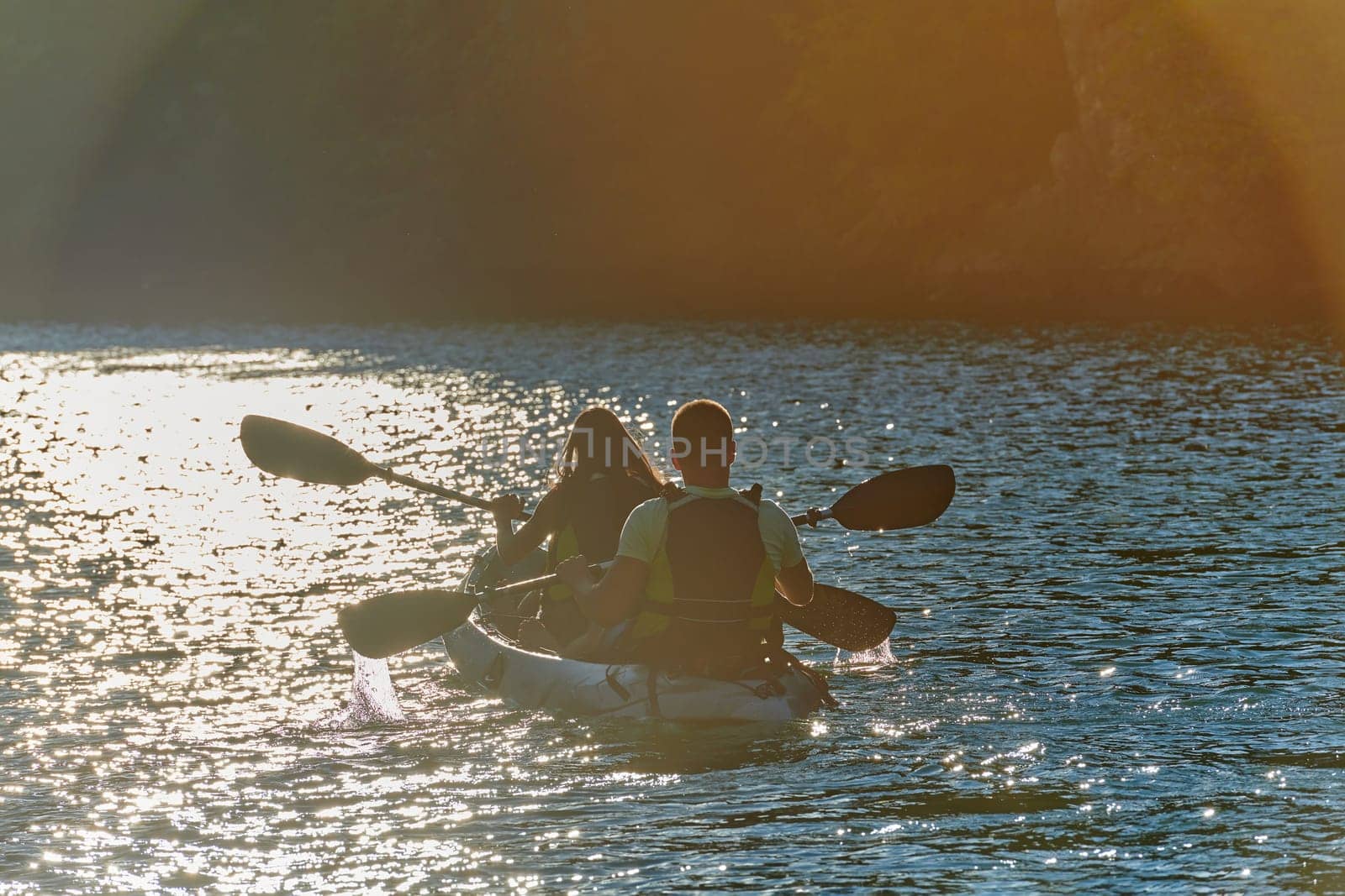 A young couple enjoying an idyllic kayak ride in the middle of a beautiful river surrounded by forest greenery in sunset time.