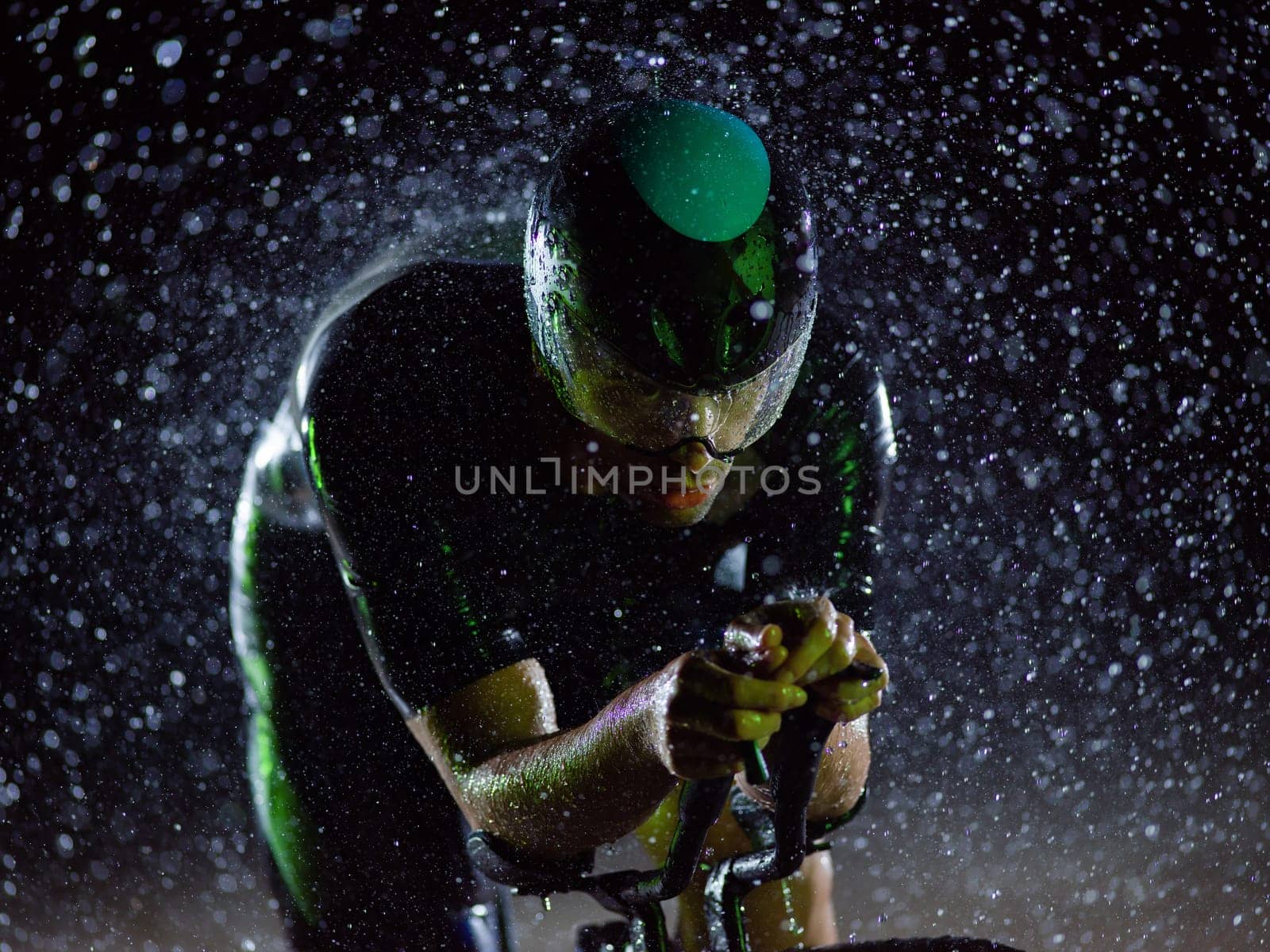 A triathlete braving the rain as he cycles through the night, preparing himself for the upcoming marathon. The blurred raindrops in the foreground and the dark, moody atmosphere in the background add to the sense of determination and grit shown by the athlete