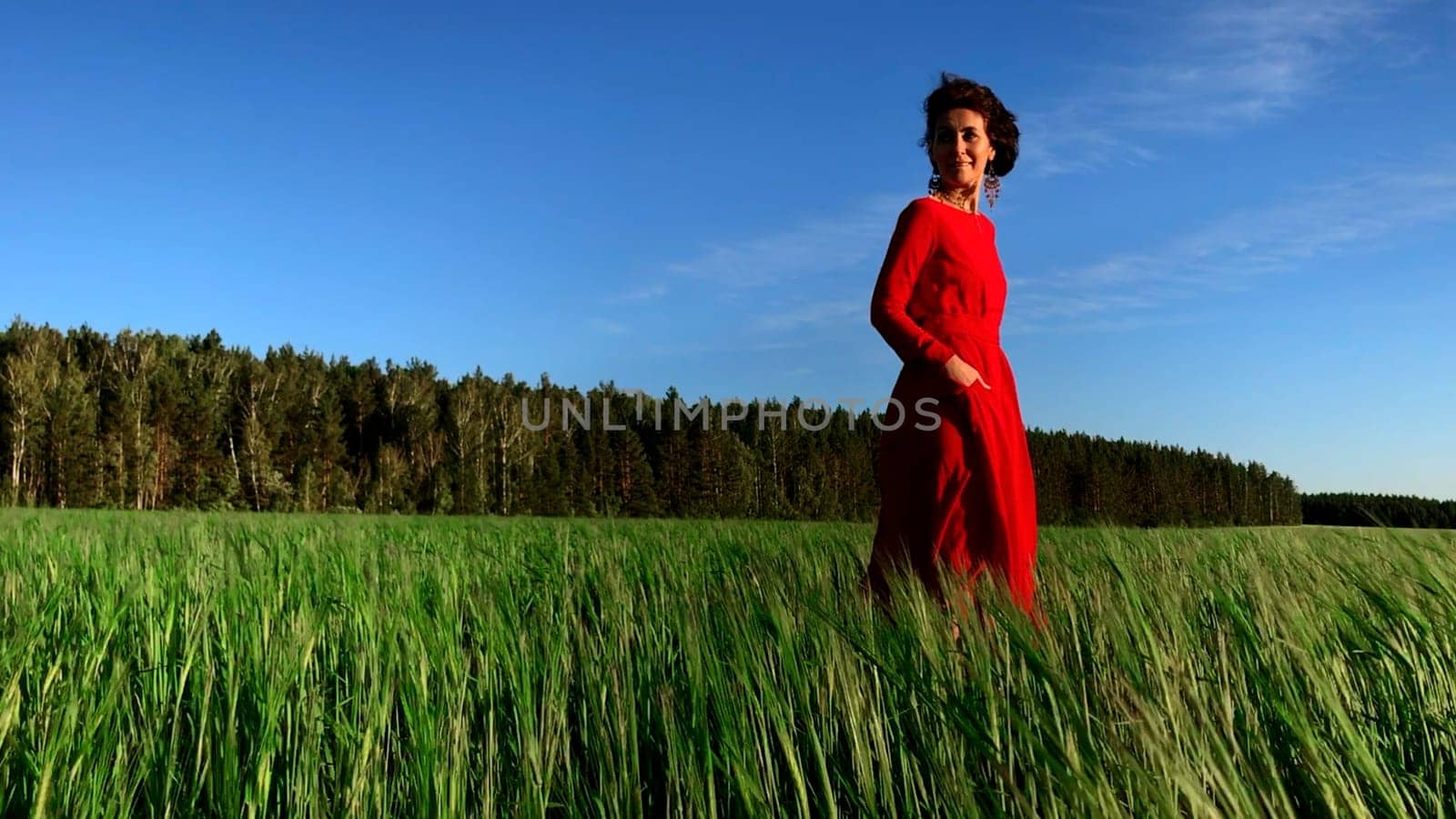 Portrait of an attractive woman in red dress in a field of fresh green wheat. Stock clip. Herbal background. amazing nature, farmland, growing cereals