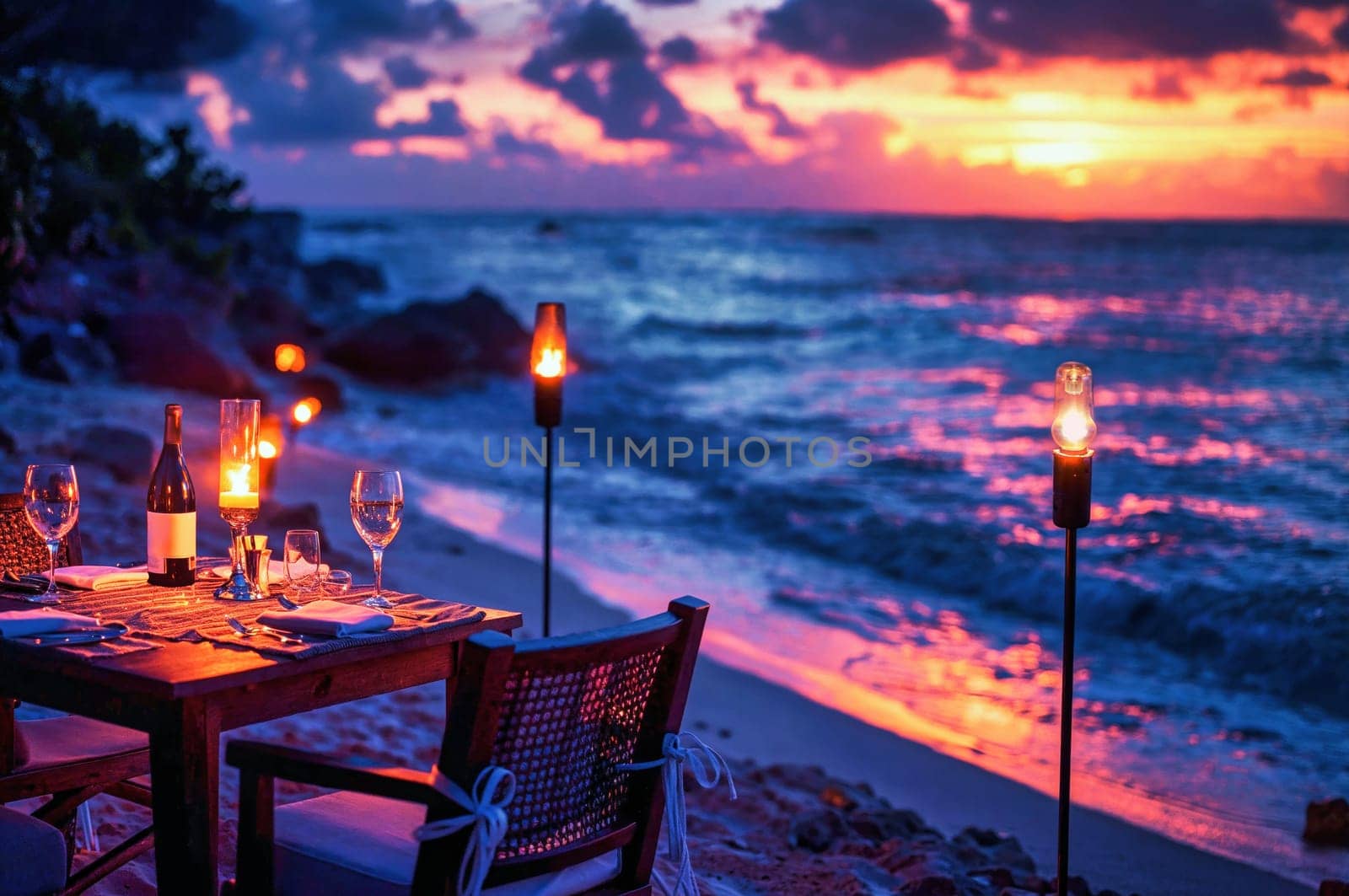 A table set for a romantic dinner on the beach with torches lit, waves gently crashing, and a stunning sunset.