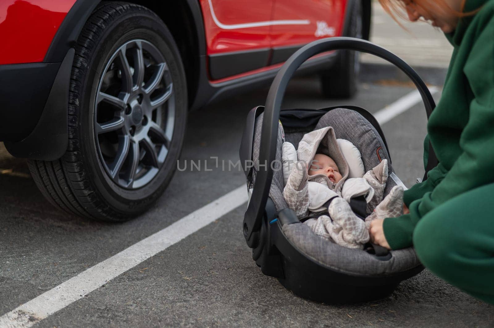 A Caucasian woman puts a child seat with a newborn baby in the car. Quick fastener