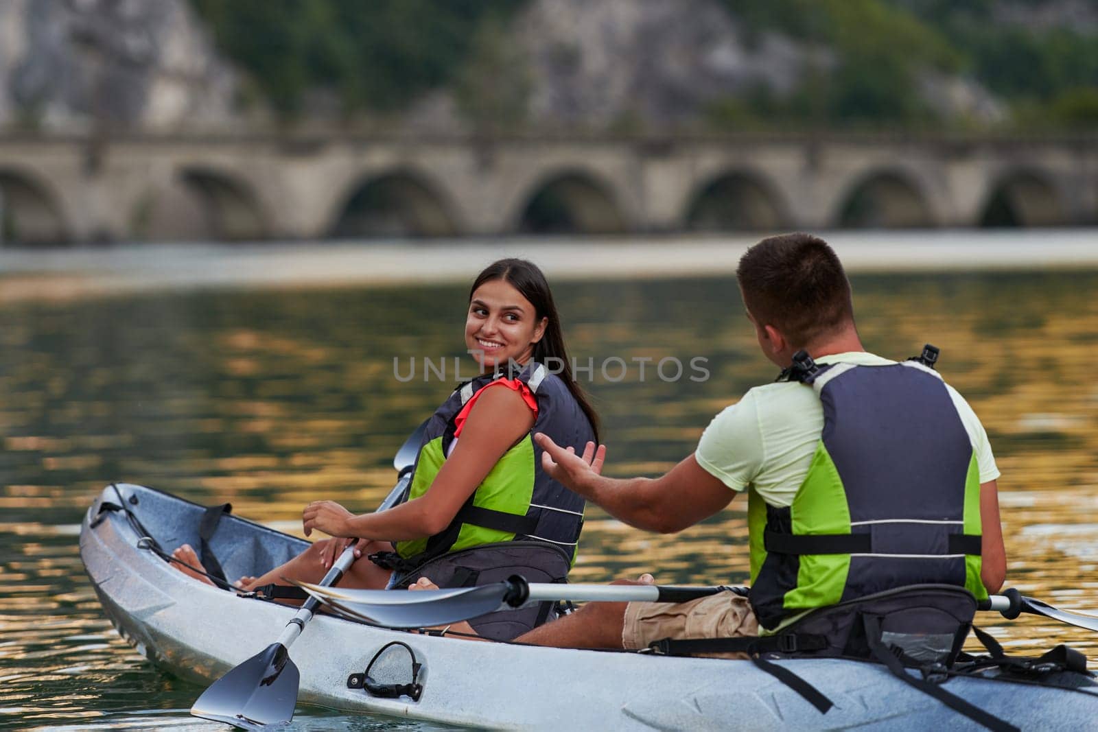 A young couple enjoying an idyllic kayak ride in the middle of a beautiful river surrounded by forest greenery by dotshock