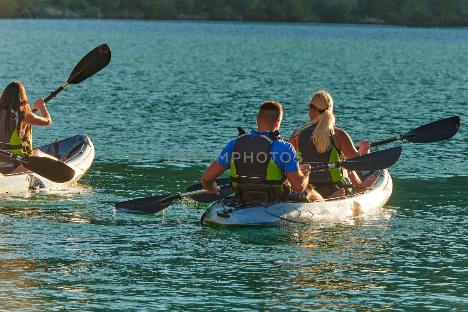 A group of friends enjoying fun and kayaking exploring the calm river, surrounding forest and large natural river canyons during an idyllic sunset