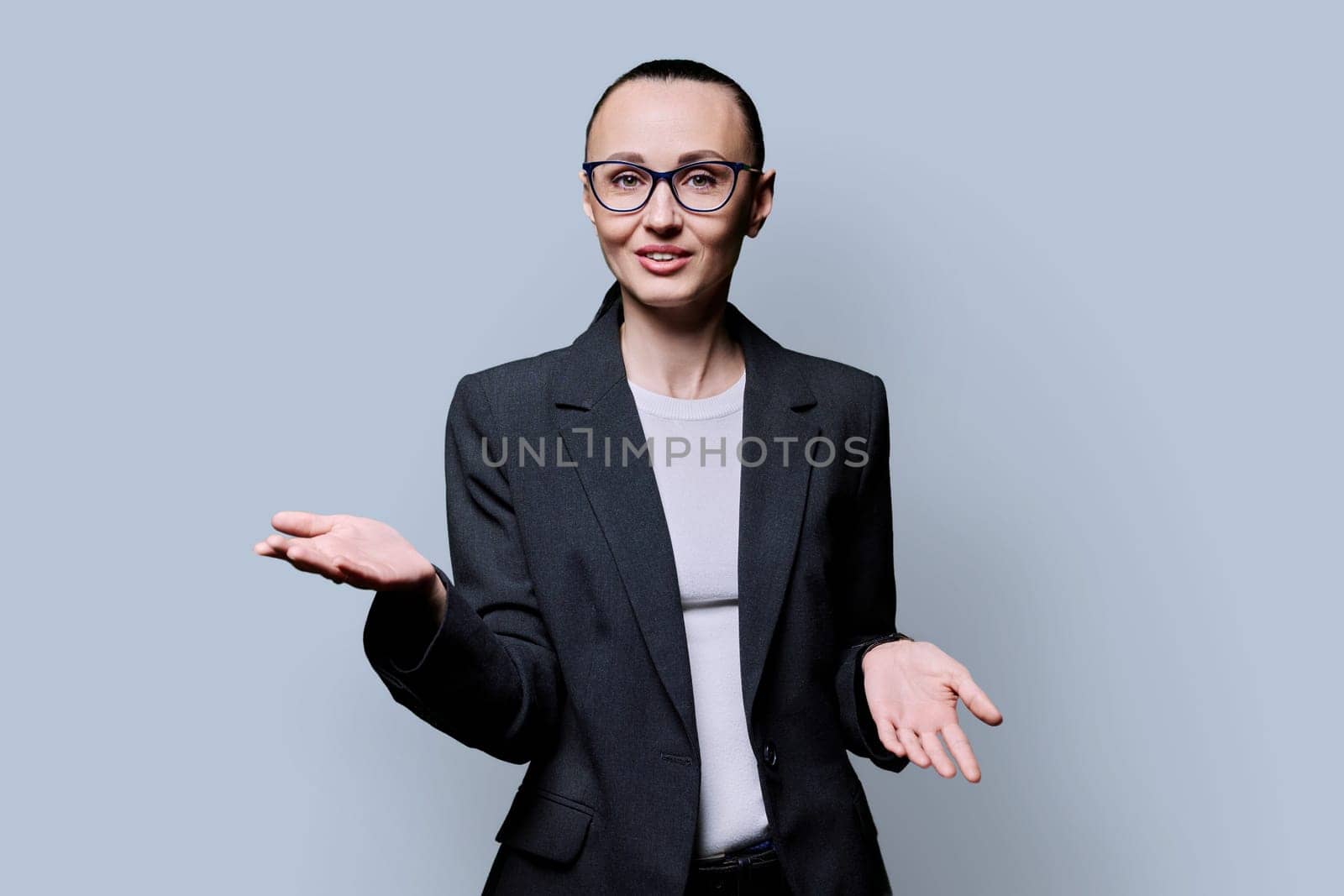 Talking friendly business middle aged elegant woman looking at camera on gray studio background. Business work job career people concept