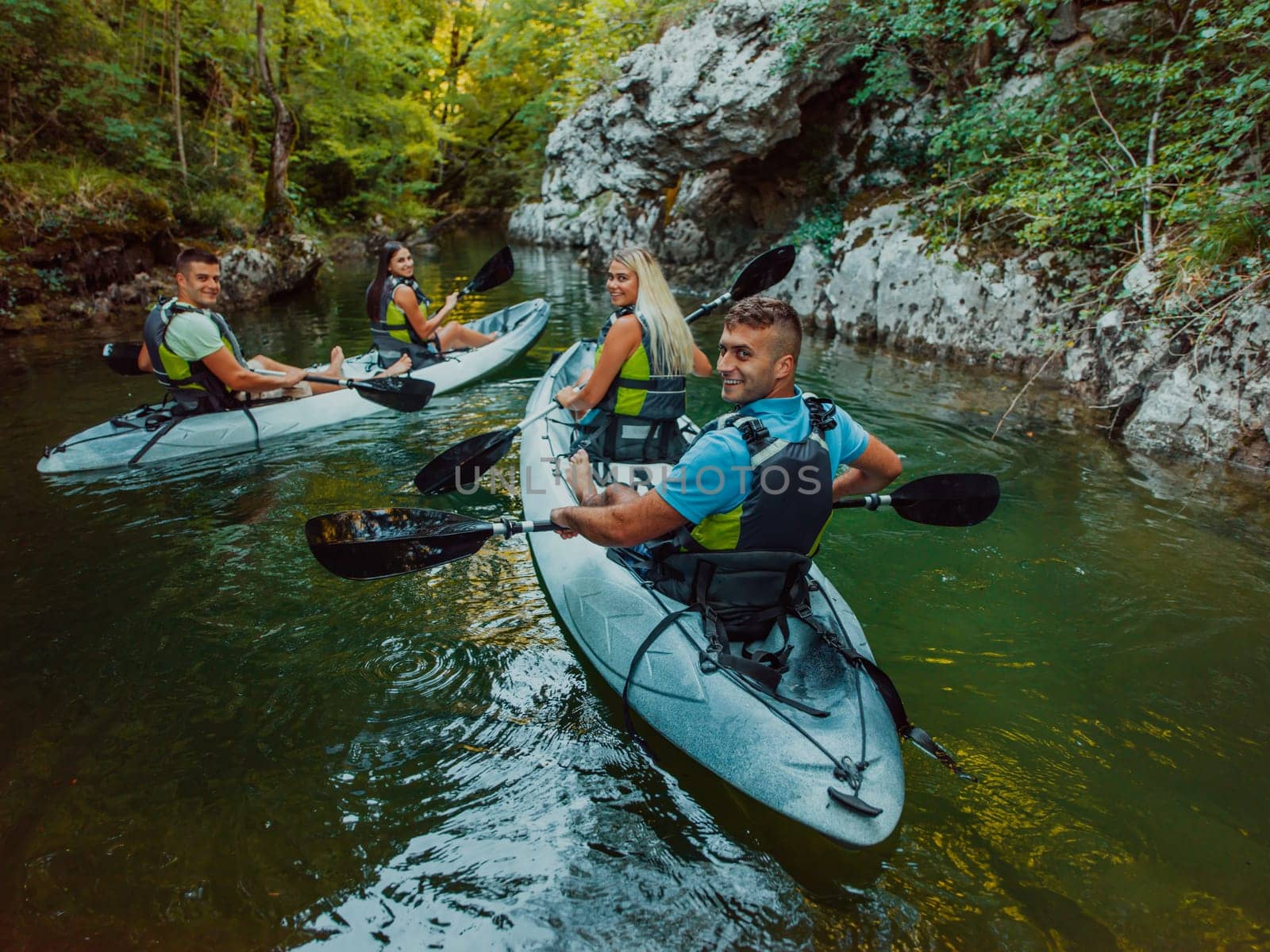 A group of friends enjoying having fun and kayaking while exploring the calm river, surrounding forest and large natural river canyons.