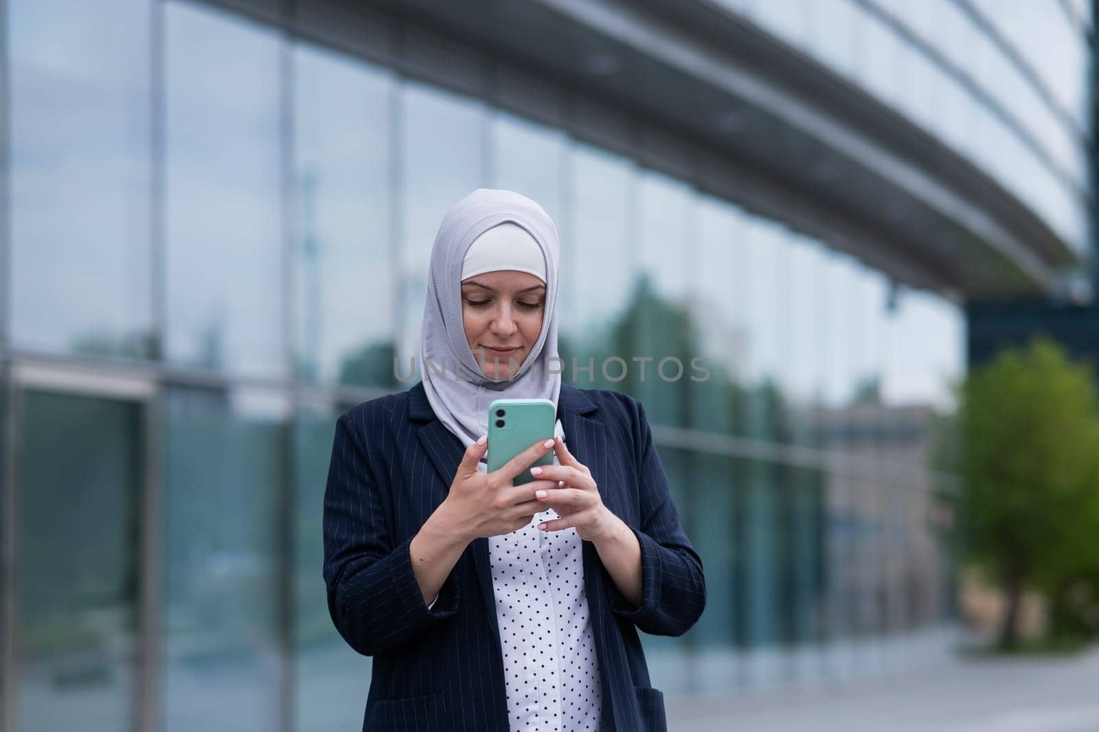 Business woman in hijab and suit using smartphone outdoors. by mrwed54