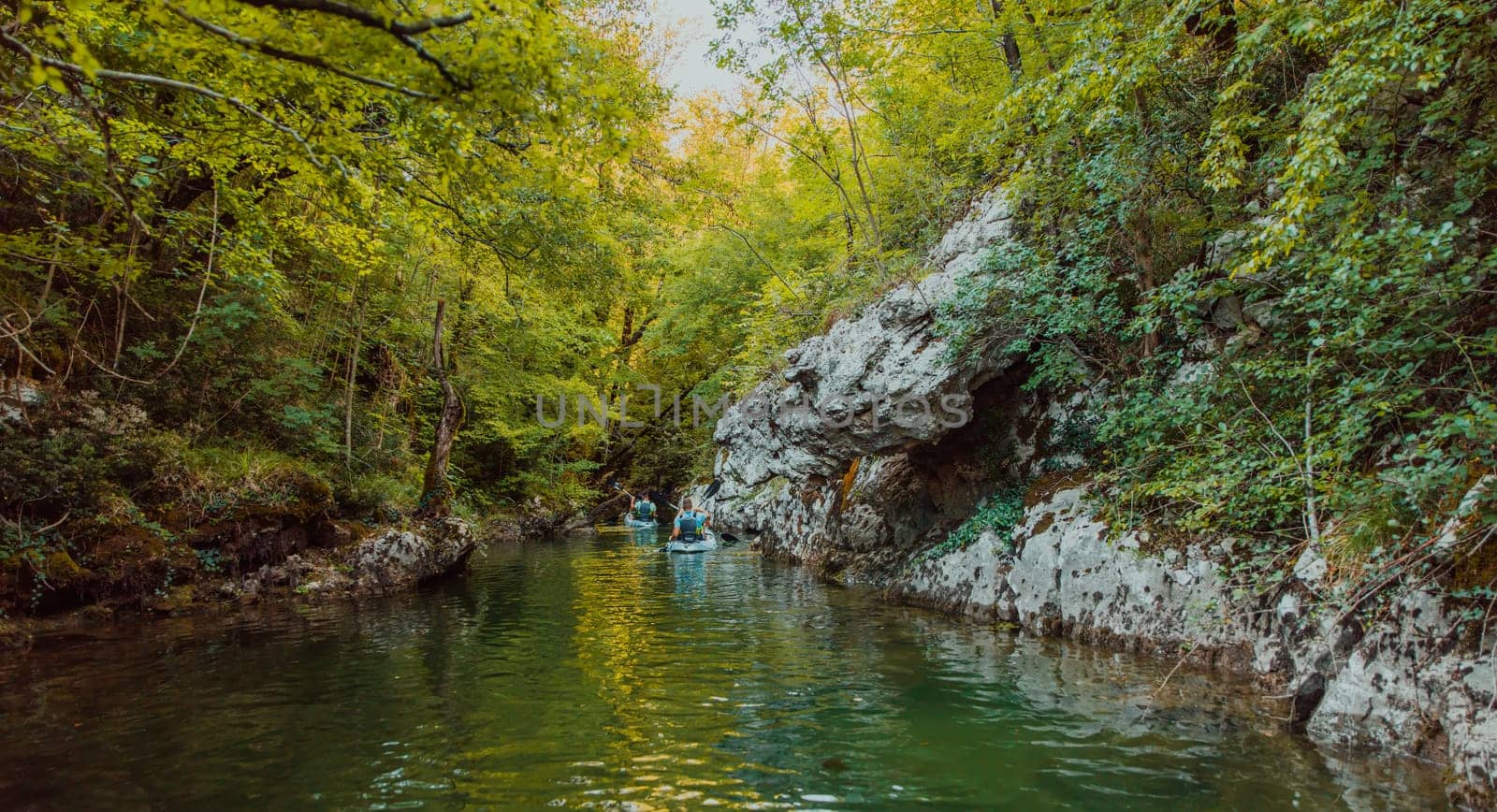 A group of friends enjoying having fun and kayaking while exploring the calm river, surrounding forest and large natural river canyons.