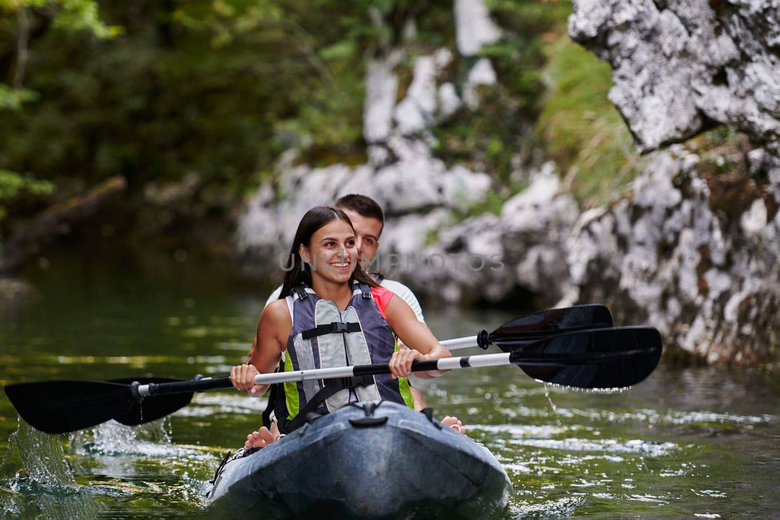 A young couple enjoying an idyllic kayak ride in the middle of a beautiful river surrounded by forest greenery by dotshock