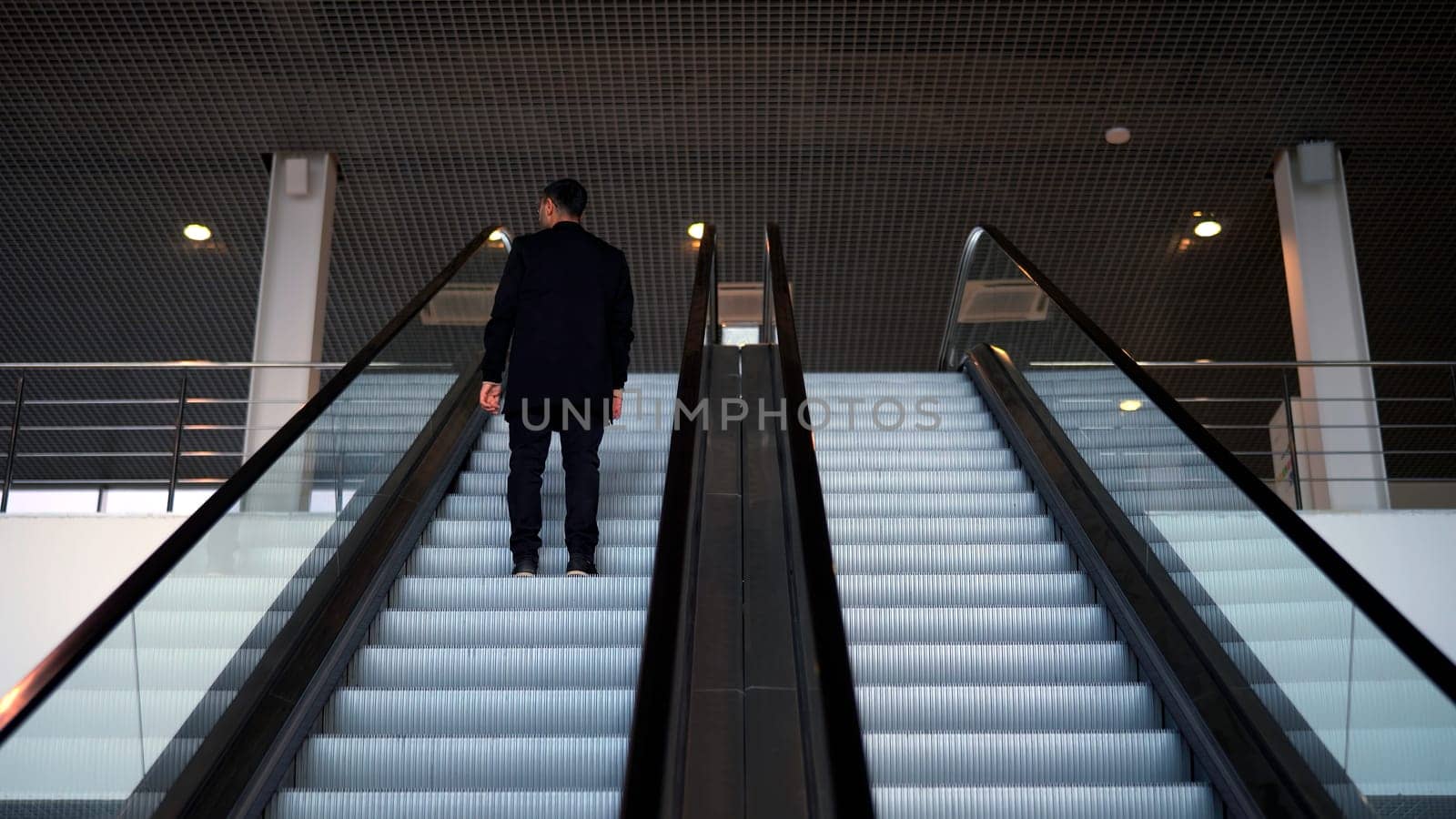 Passenger riding on the escalator up to the station of the ground metro. Media. Rear view of a young businessman on the escalator