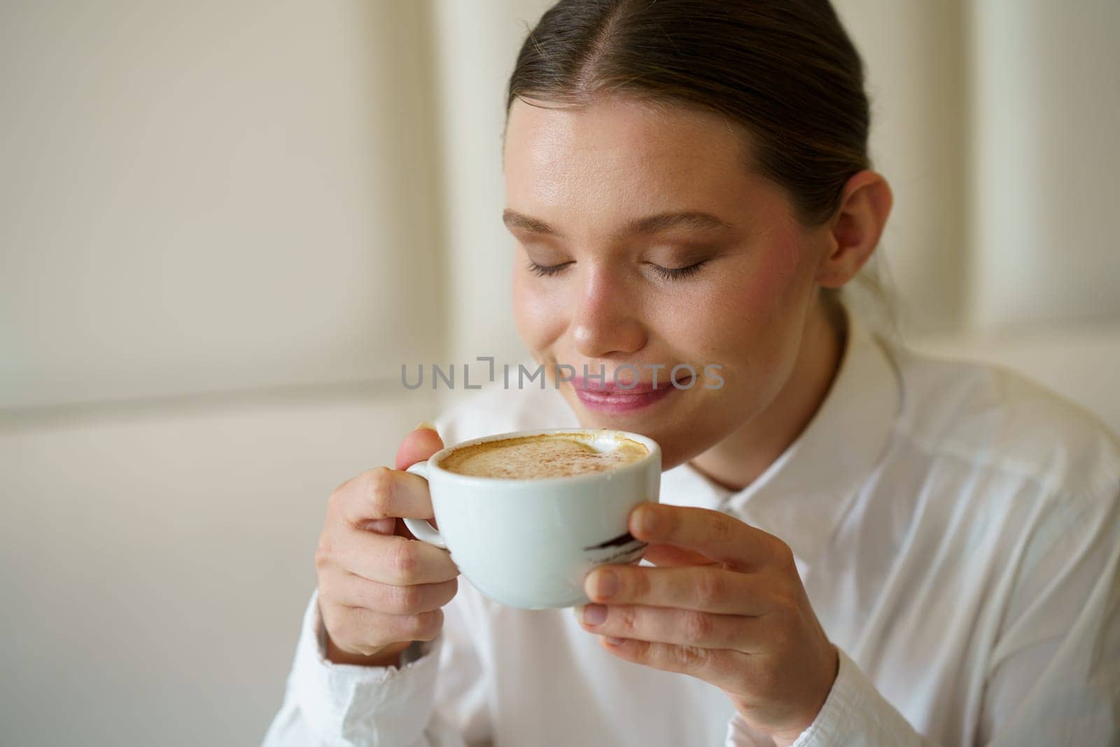 Close-up of an elegant beauty adult caucasian woman smelling a delicious coffee in a modern cafeteria