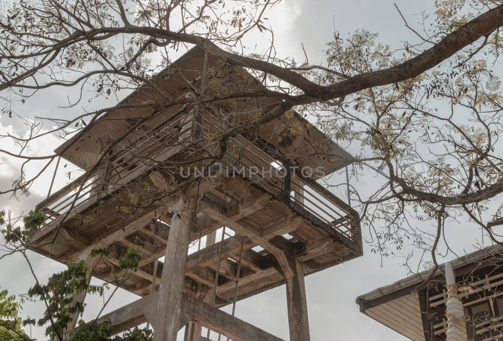 Bottom up view of Branches of tree in front of Old water tower made of Cement and metal staircase with sky background. Selective focus. Selective focus.