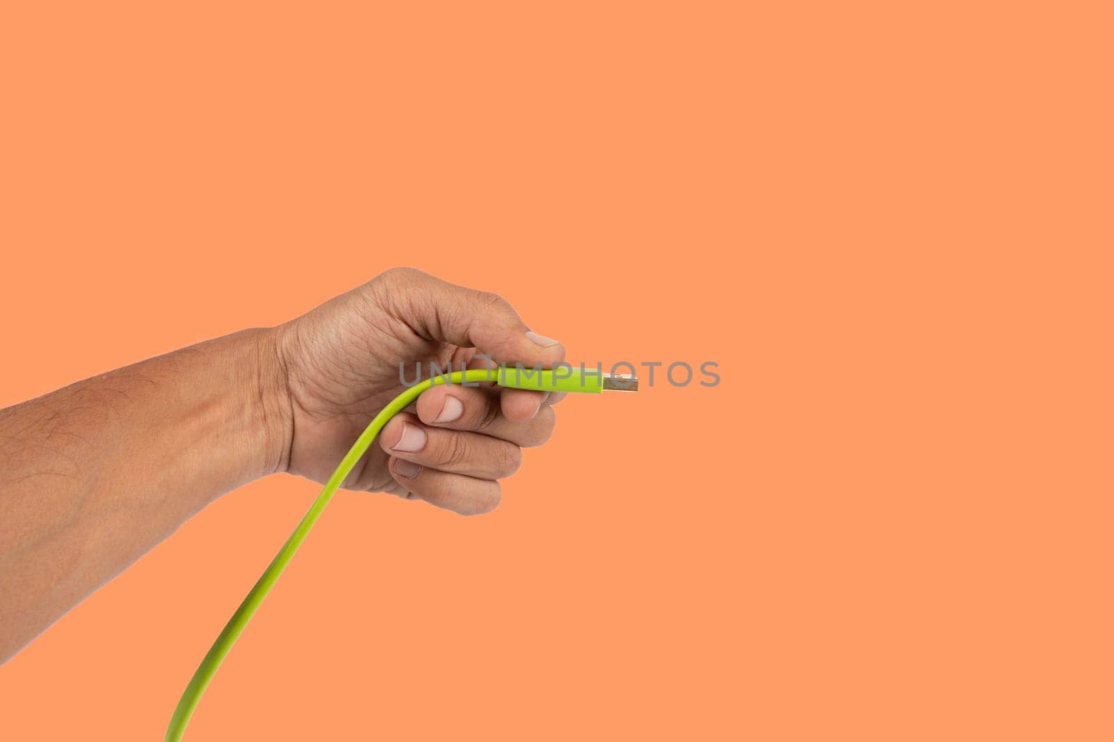 Black male hand holding a green USB cable isolated on orange background. High quality photo