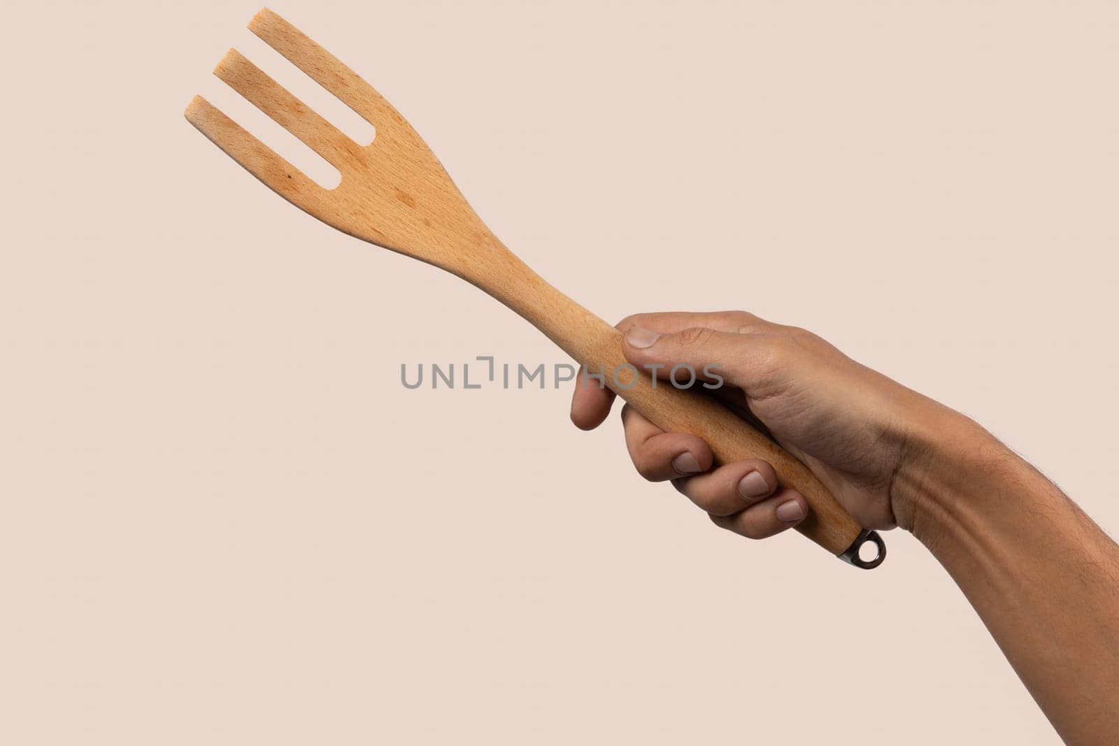 Hand holding wooden fork on beige background cutout. High quality photo