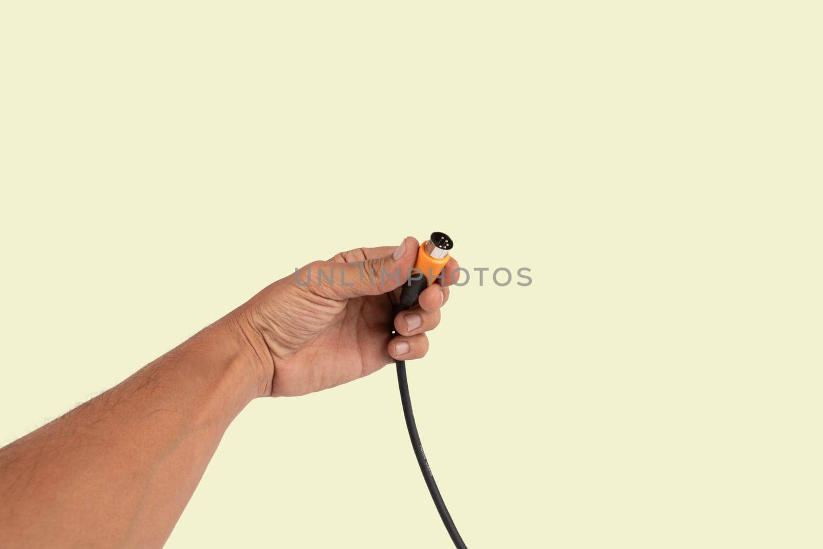 Black male hand holding a MIDI audio cable isolated light on green background. High quality photo