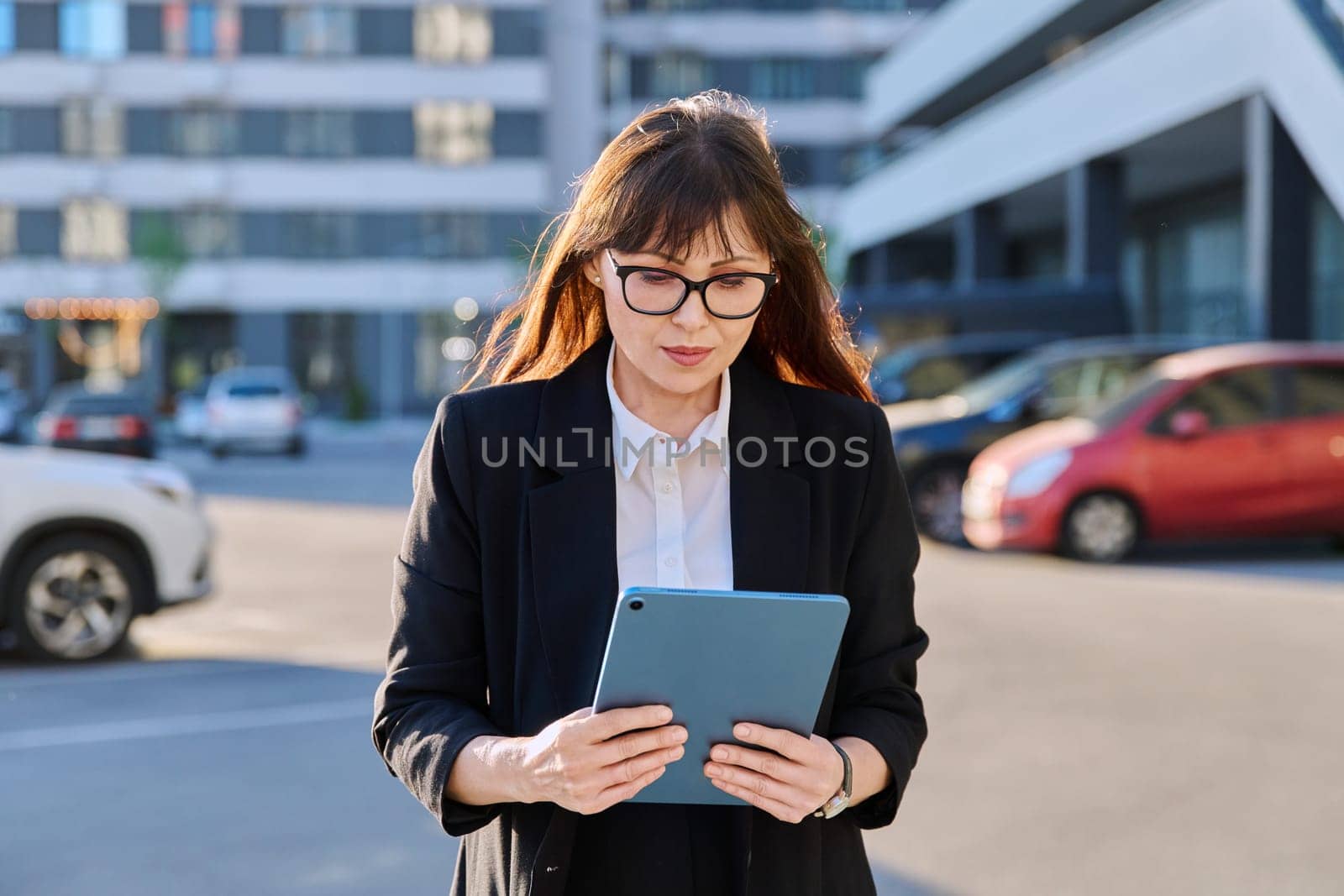 Mature woman manager professional agent entrepreneur using digital tablet for work, modern city. Female leader businesswoman in business suit, outdoor, internet software applications apps technology