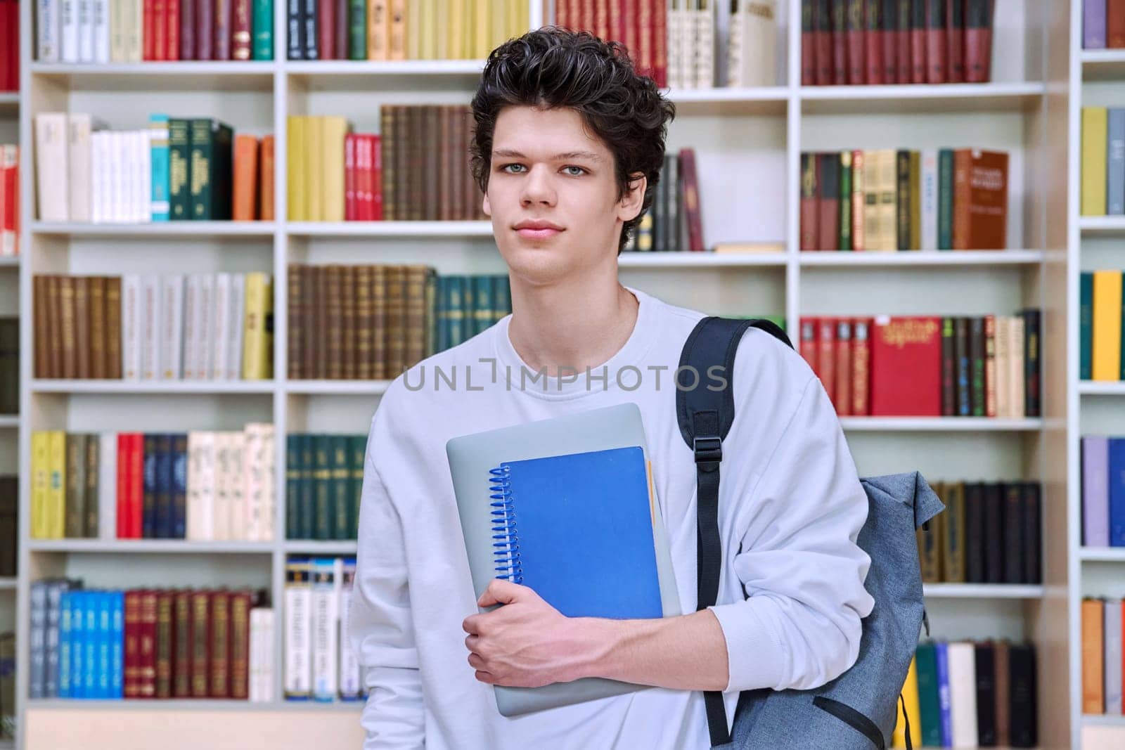 Portrait of confident handsome college student teenage male 19, 20 years old inside library of educational building. Education, youth, lifestyle concept