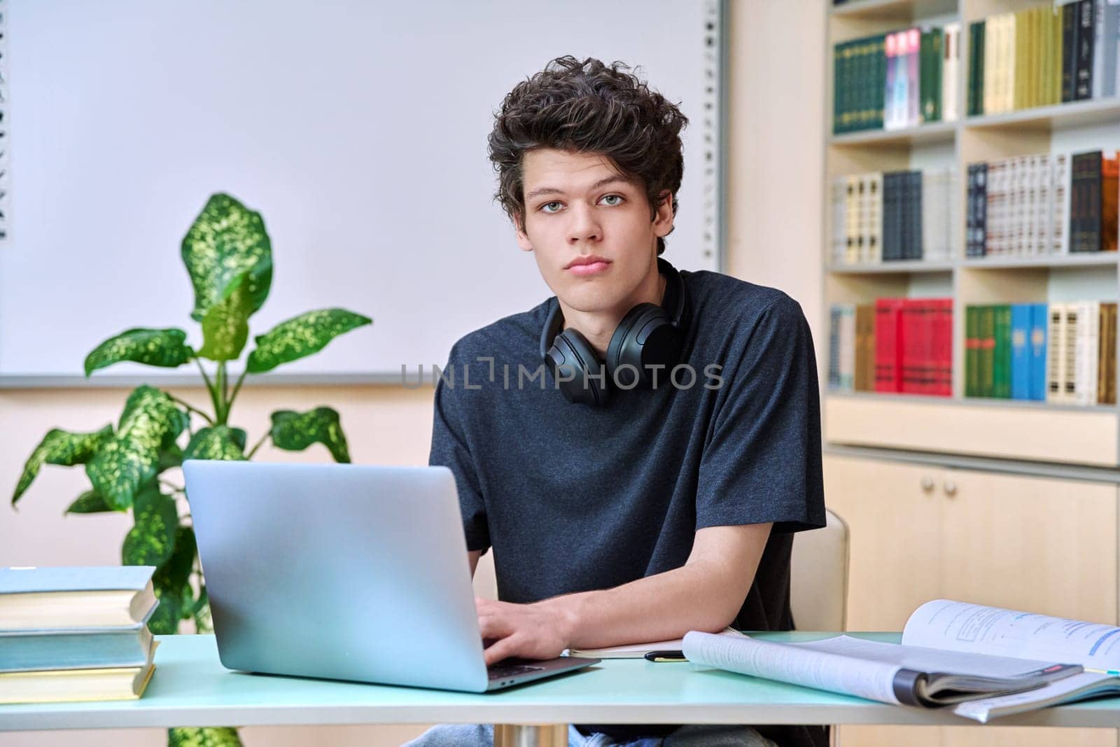 Portrait of college student guy sitting at desk with laptop computer and textbooks inside educational library classroom. Education internet technology e-learning learning services applications youth