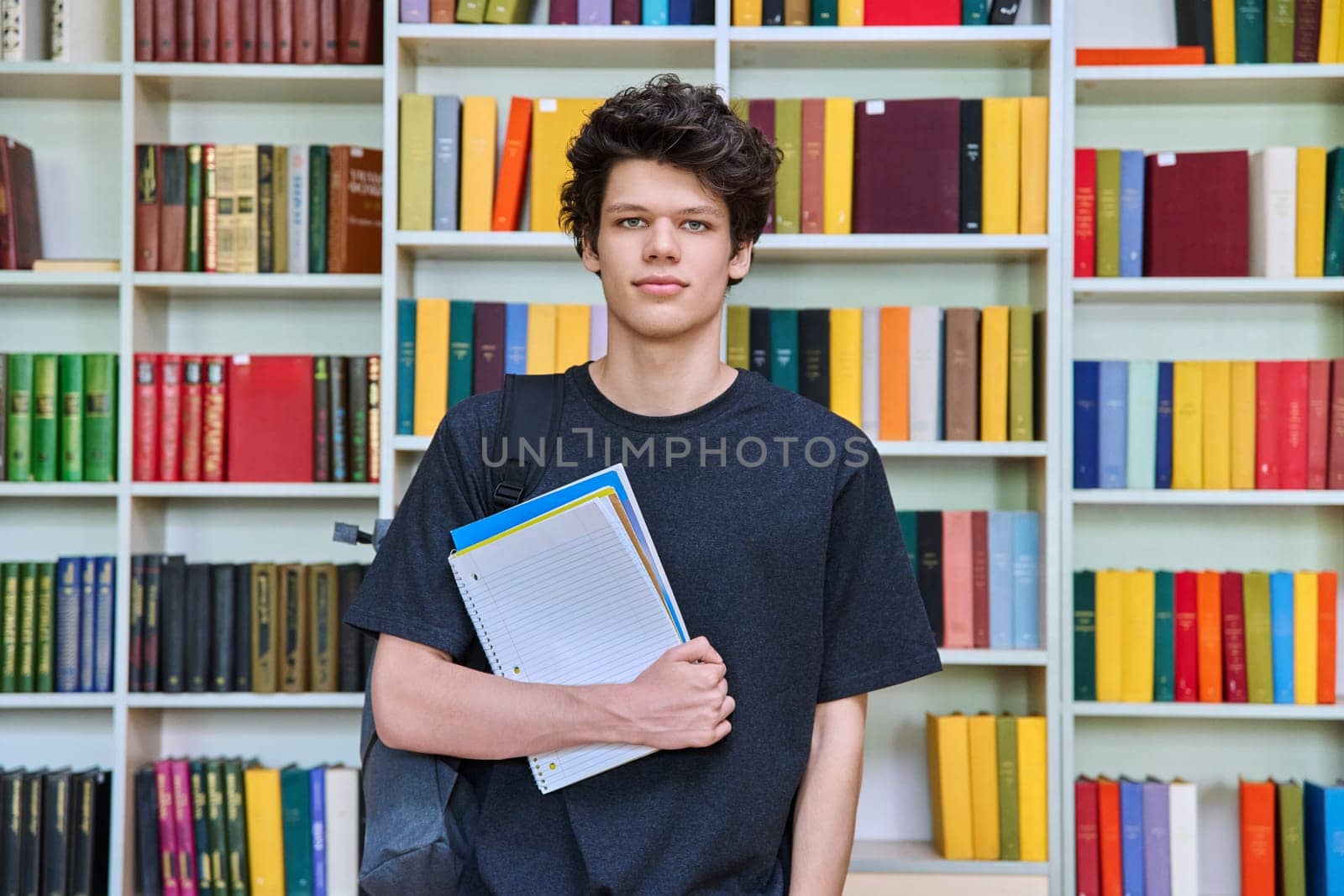 Portrait of confident handsome college student teenage male 19, 20 years old inside library of educational building. Education, youth, lifestyle concept