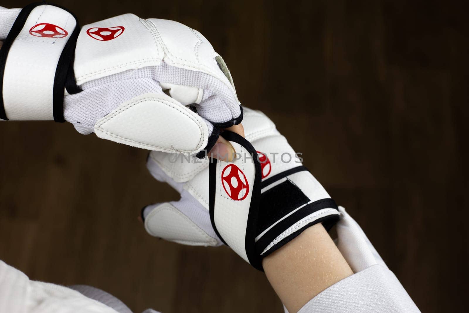 Girl fixes protective Kyokushinkai karate gloves with Velcro on her wrist, protection by martial arts athlete, putting on karate equipment