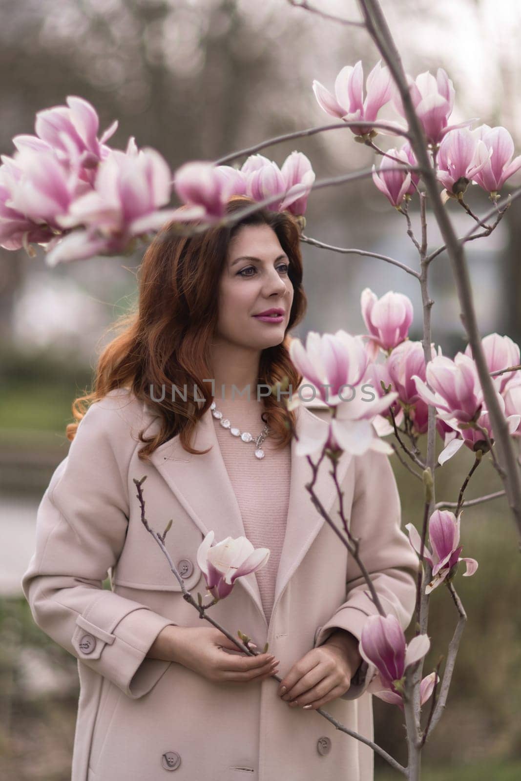 Woman magnolia flowers, surrounded by blossoming trees, hair down, wearing a light coat. Captured during spring, showcasing natural beauty and seasonal change