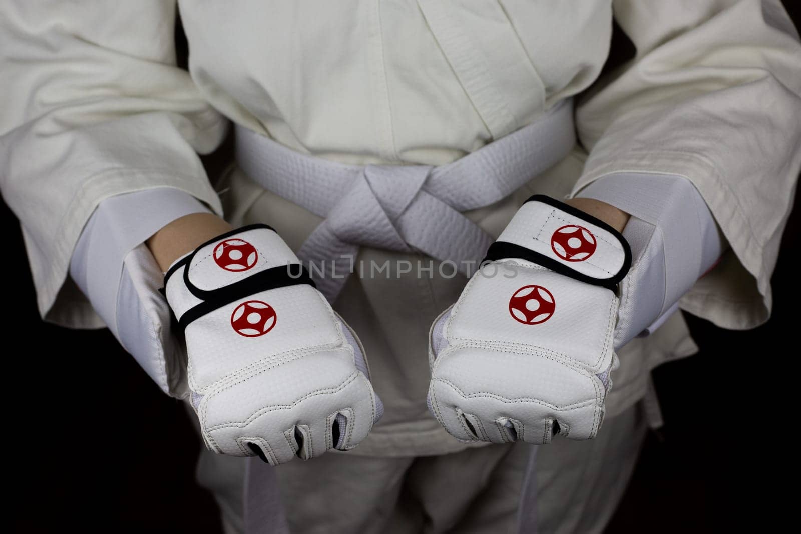 Young woman in kimono and white belt shows clenched fists in protective gloves in Kyokushin karate, combat equipment and protection of a martial arts athlete