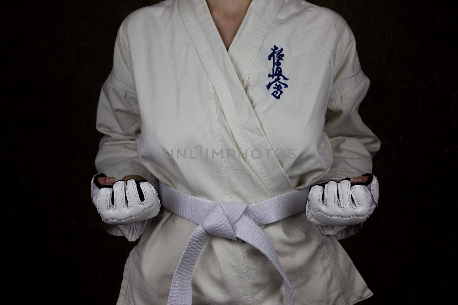 Girl athlete in kimono and white belt in Kyokushin karate stands in stance with clenched fists with reverse grip, concept of karate athlete. Inscription in Japanese: Kyokushinkai