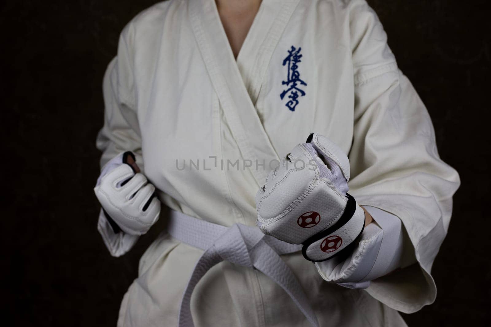 Young woman in Kyokushin karate kimono in fighting stance with lowered clenched fists by timurmalazoniia