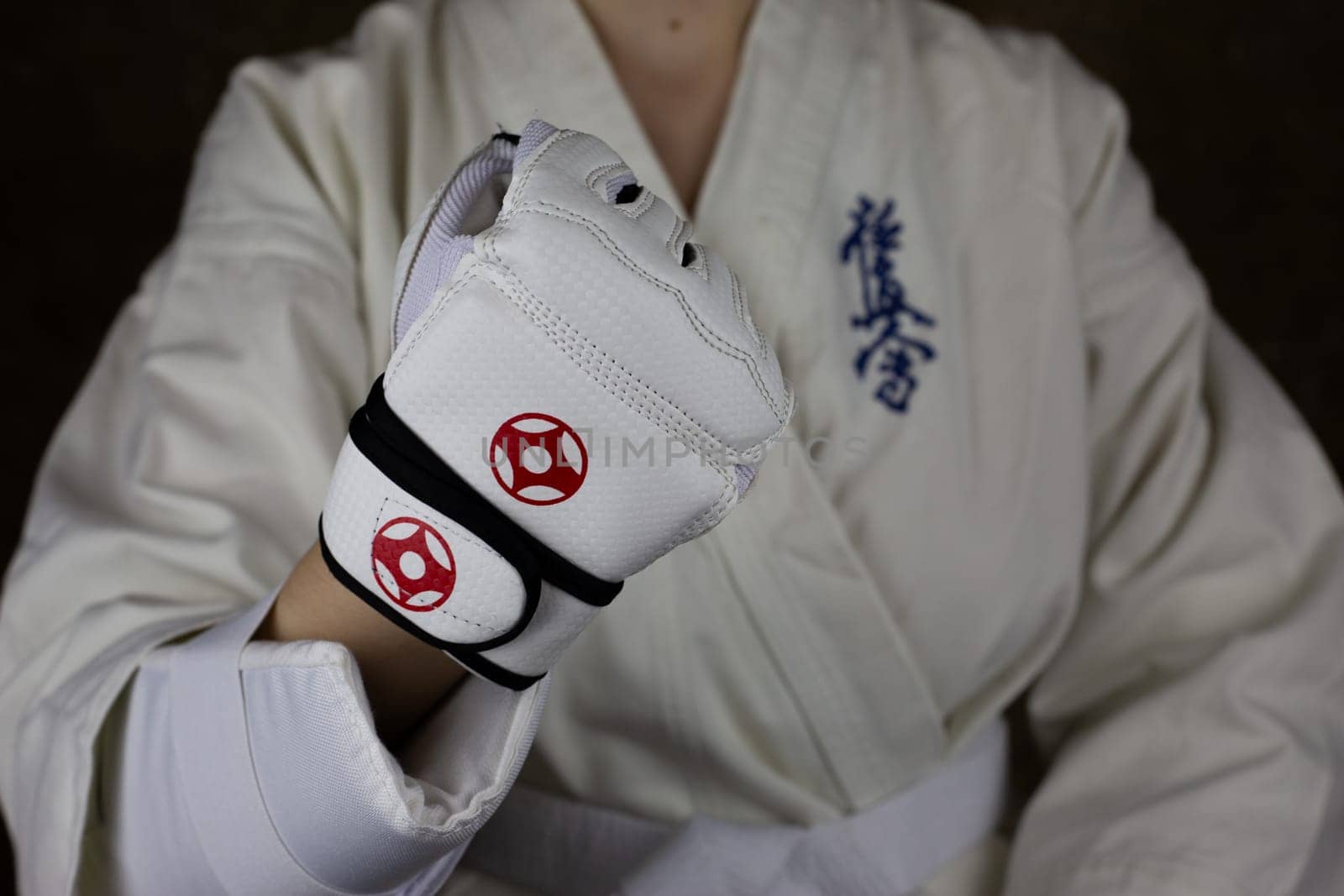 Girl athlete in Kyokushinkai karate demonstrates clenched fist in special protective glove for martial arts. Athlete in karate kimono. Inscription in Japanese: Kyokushinkai