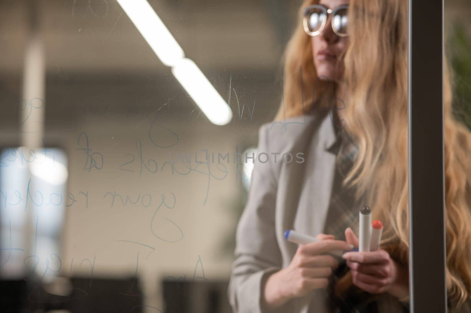 Caucasian woman with glasses writes text in English on a glass wall. by mrwed54