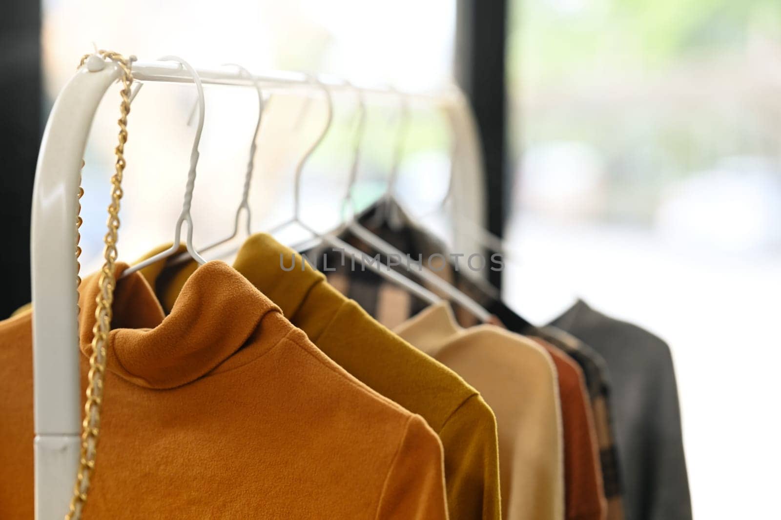New collection of warm tones stylish clothes hanging on a rail in fashion design studio.