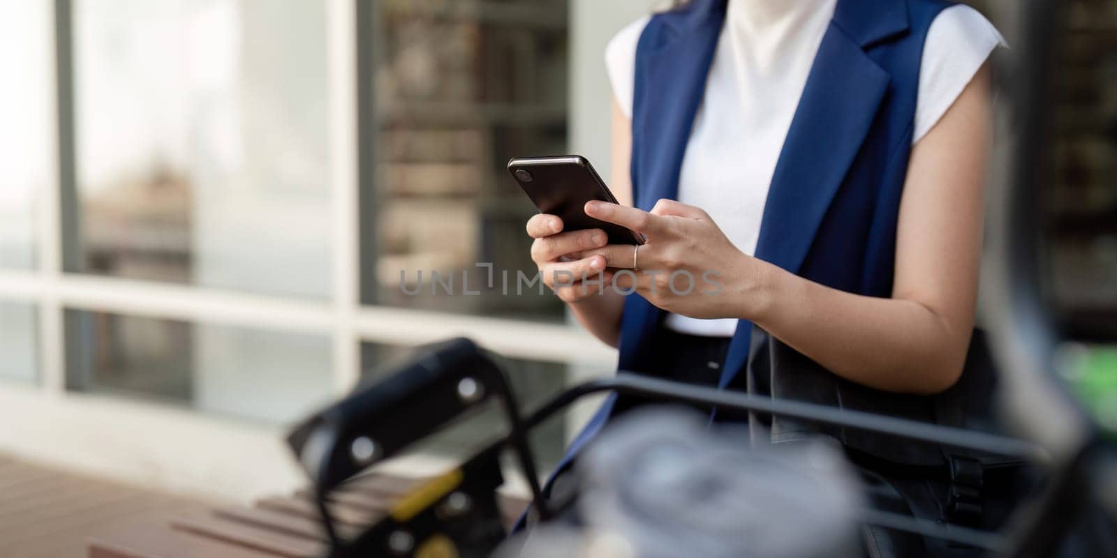 Businesswoman using smartphone while commuting by bicycle outside office. Concept of modern communication, connectivity, and sustainable transport.